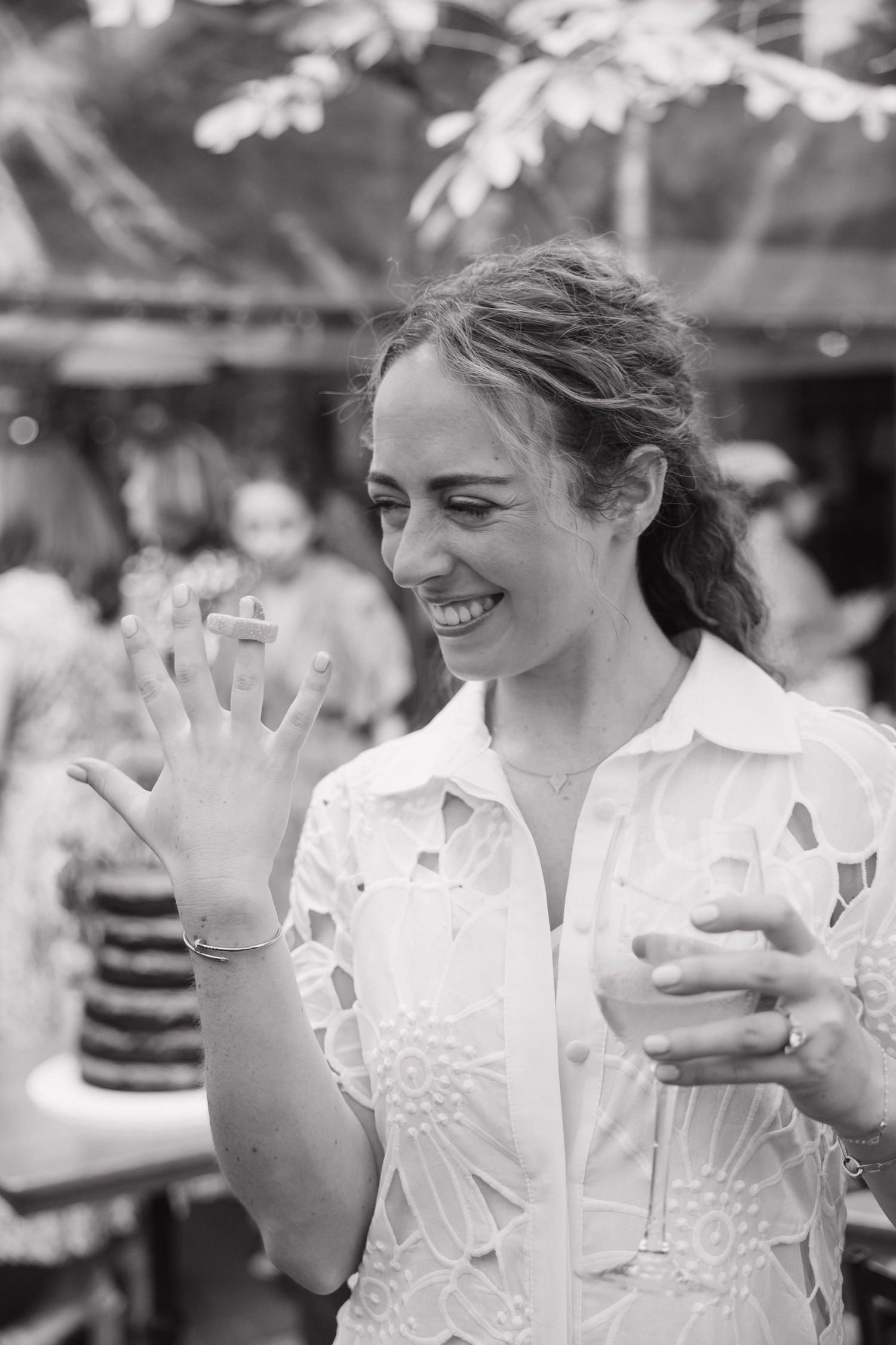 Happy woman in white lace shirt smiling and showing engagement ring, black and white.