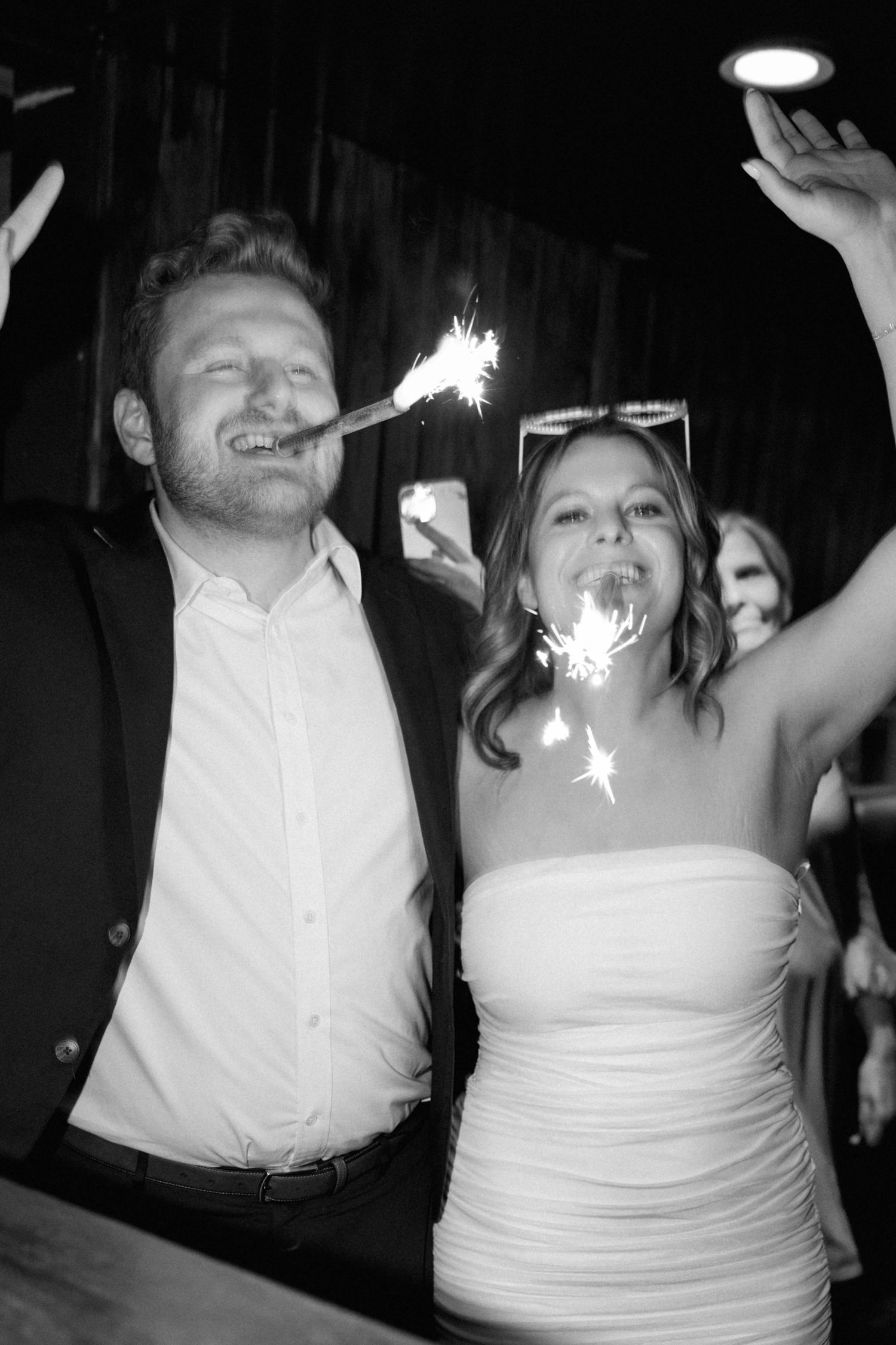 Black and white photo of couple holding sparklers and celebrating at wedding reception.