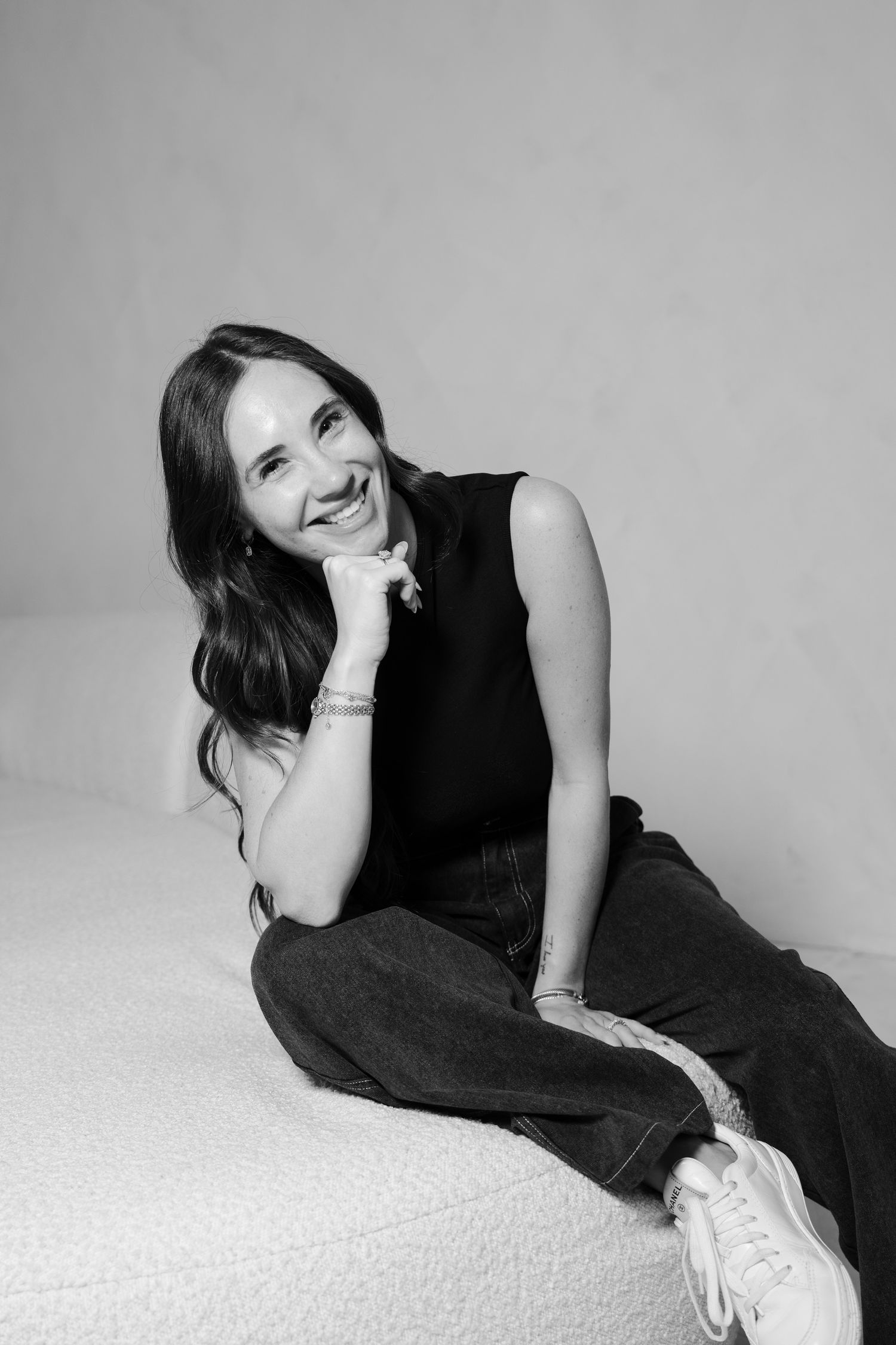Black and white portrait of a smiling brunette woman sitting casually on a white couch.