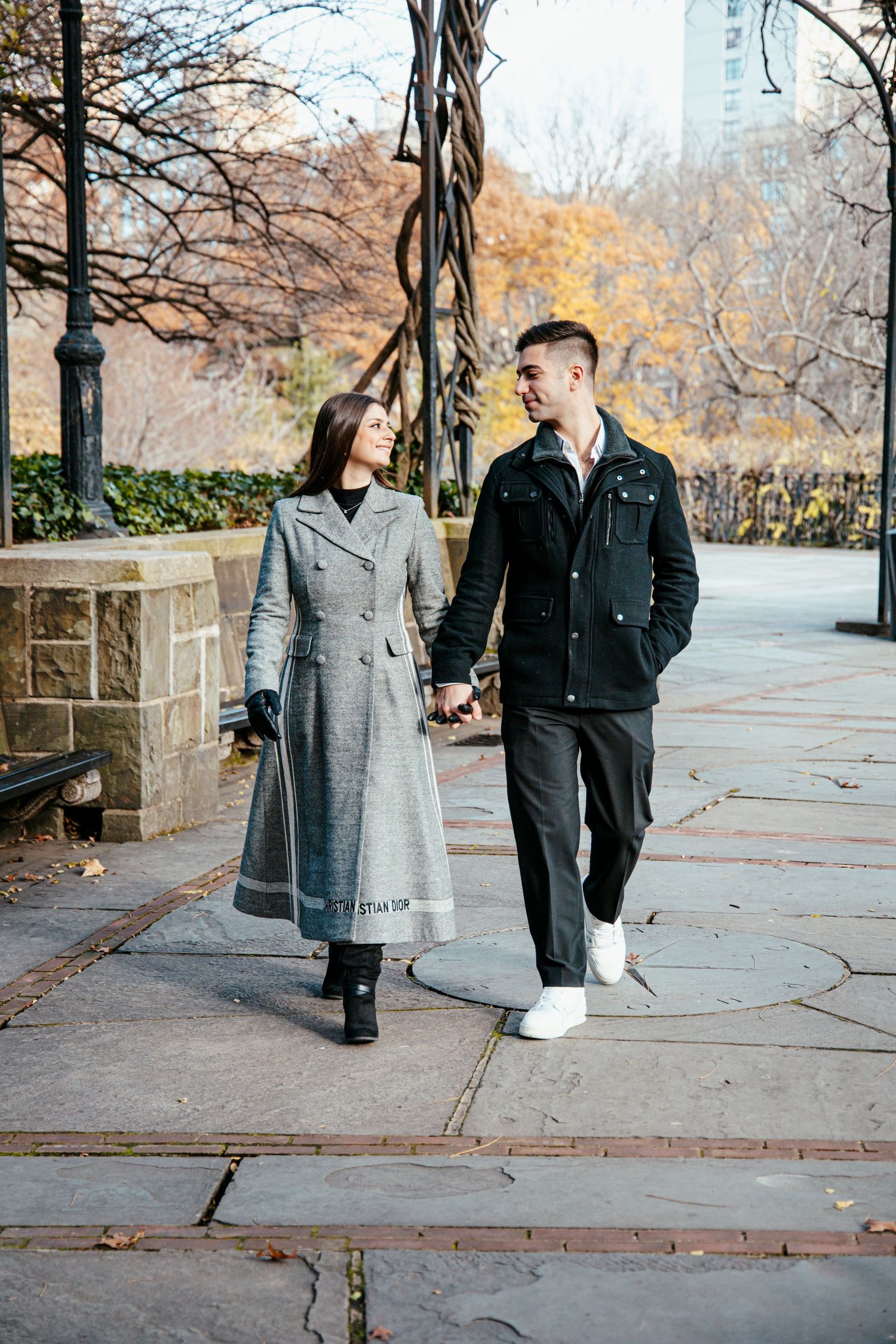Happy couple walking hand-in-hand through Central Park in autumn wearing stylish winter coats.