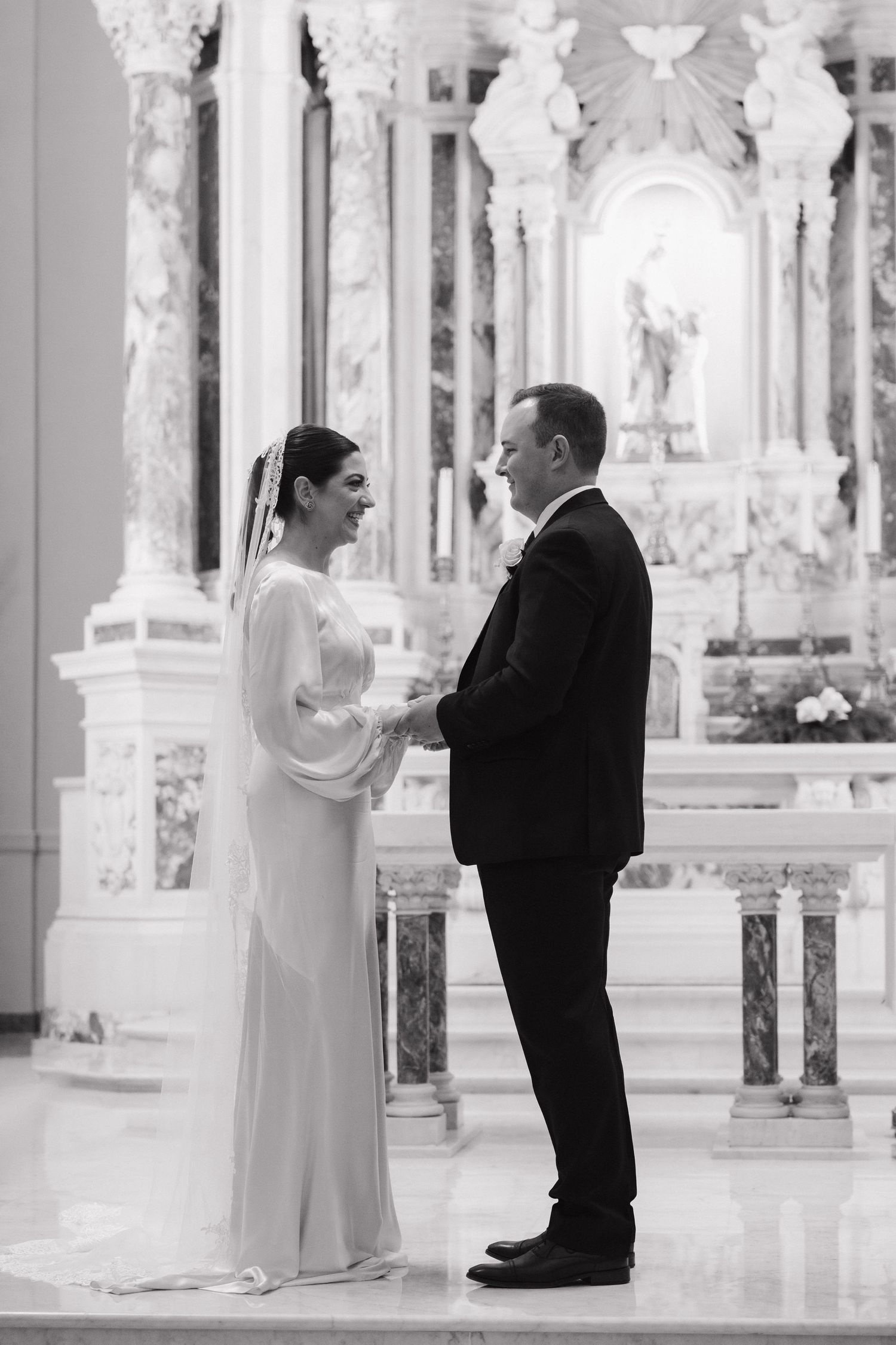 Bride and groom exchanging vows at ornate church altar in black and white.