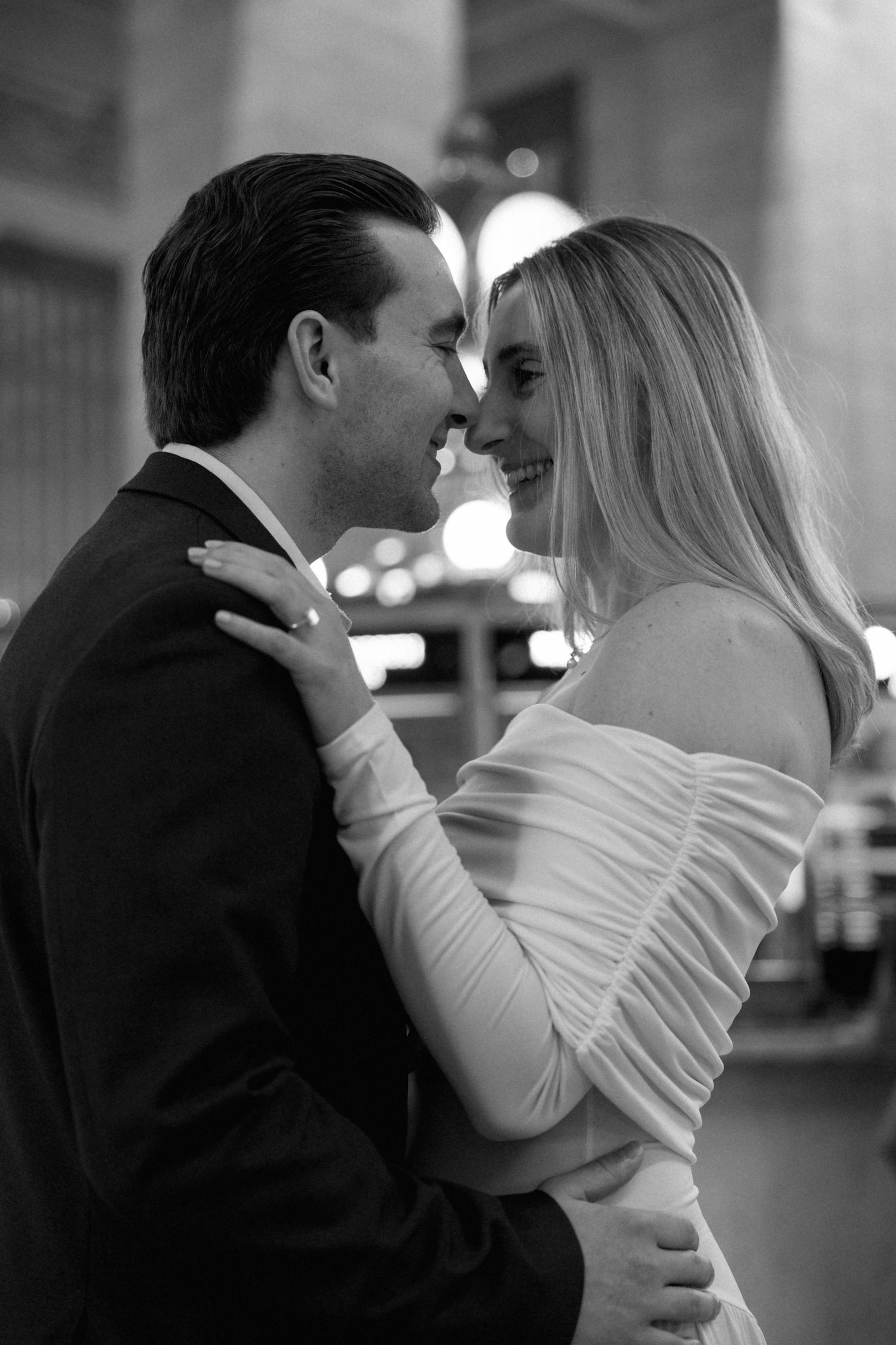 Black and white romantic portrait of an elegantly dressed couple smiling face to face.