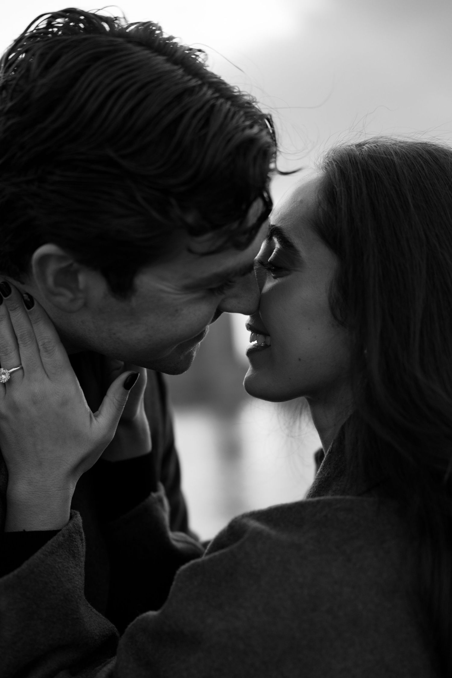 Intimate black and white close-up of couple touching foreheads, woman showing diamond engagement ring.