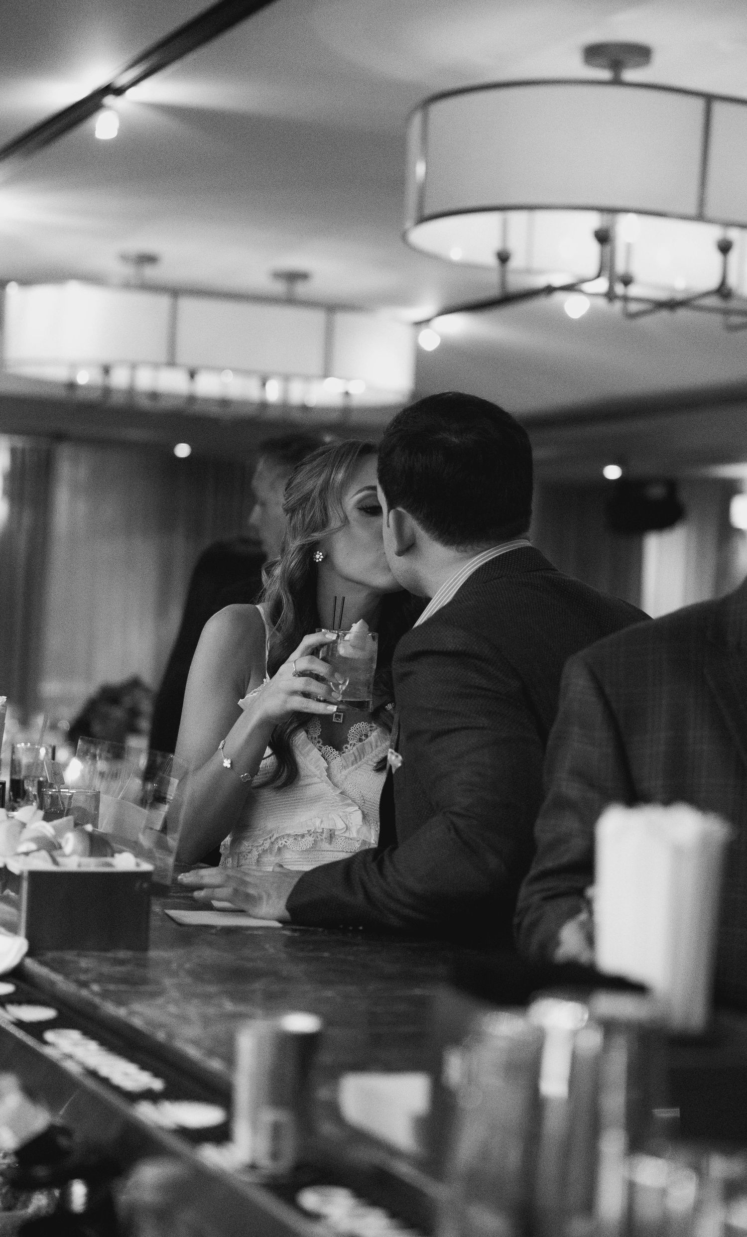 Black and white photo of couple sharing a kiss at a bar during an elegant indoor reception.