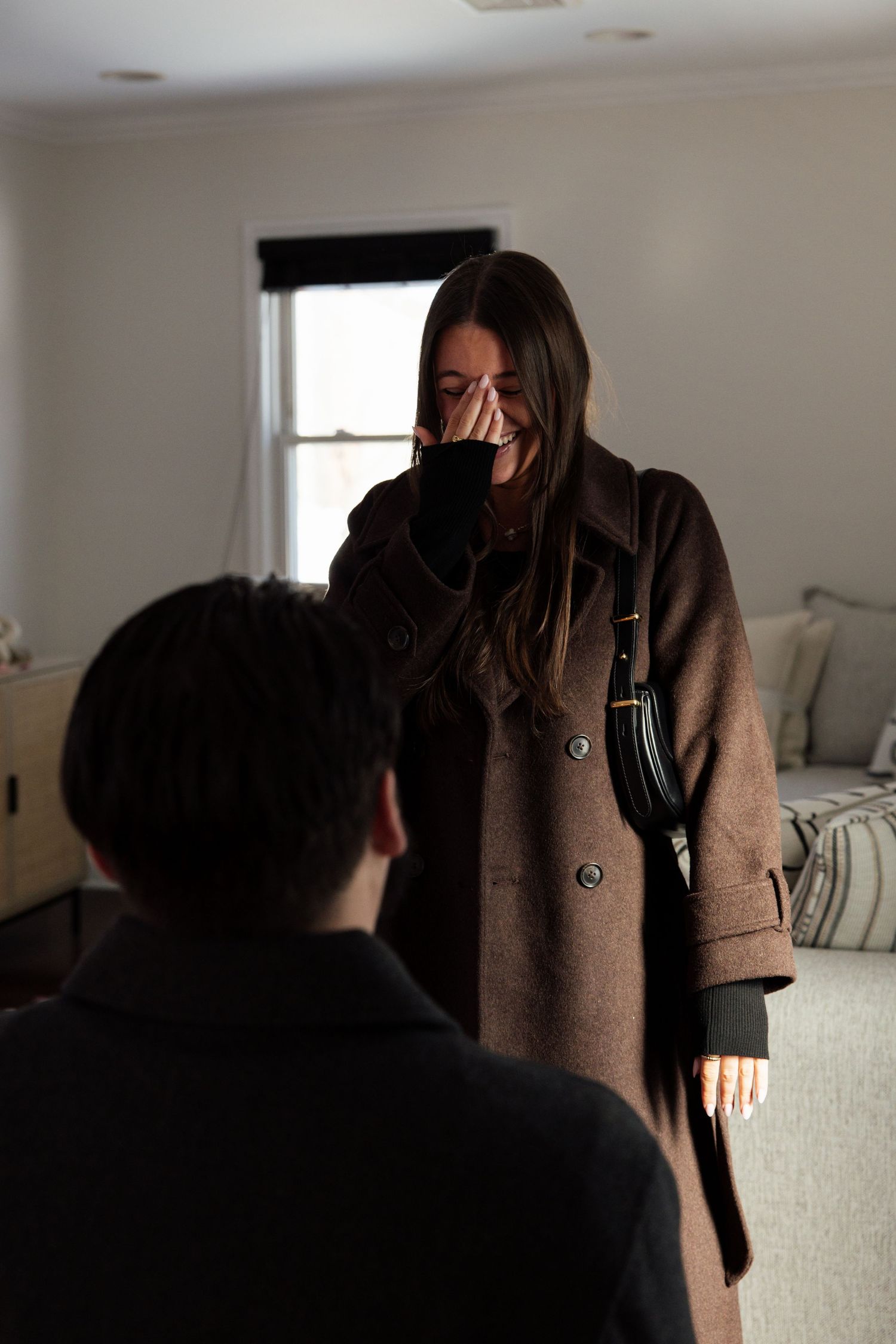 Emotional woman covering her face during an indoor marriage proposal moment at home.
