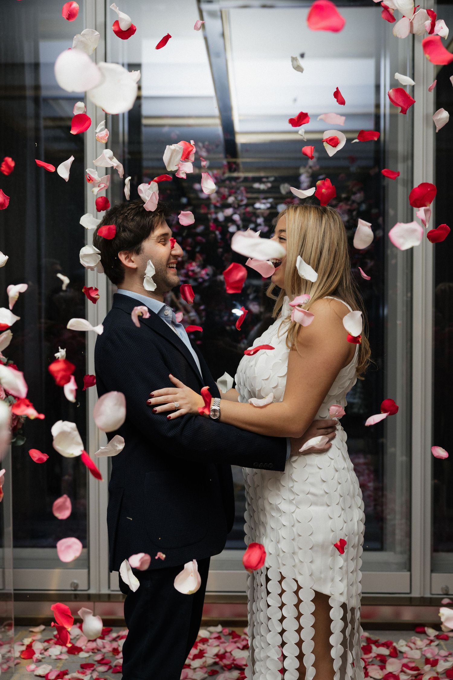 Joyful couple embracing in shower of red and white rose petals during wedding celebration.