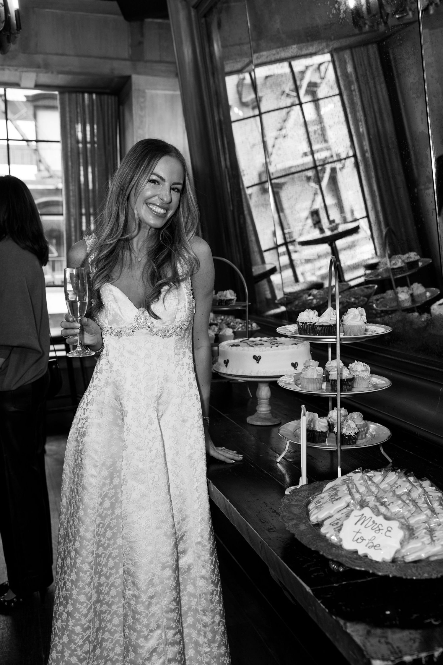 Smiling bride in a white wedding gown standing near a dessert table at her wedding reception.