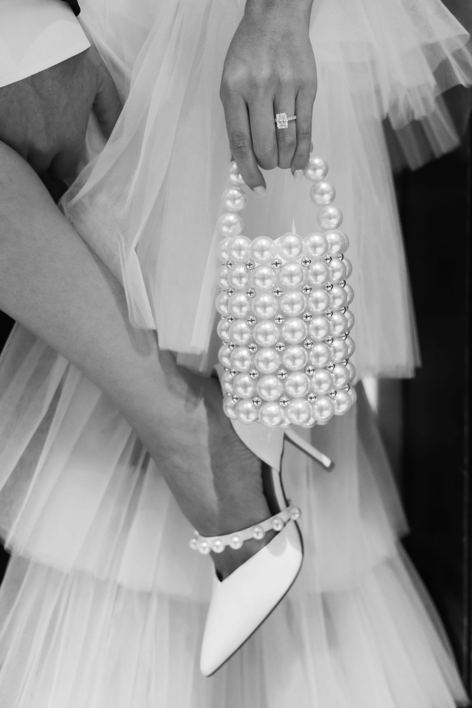 Black and white close-up of bride holding pearl bag wearing pearl-adorned wedding heels.