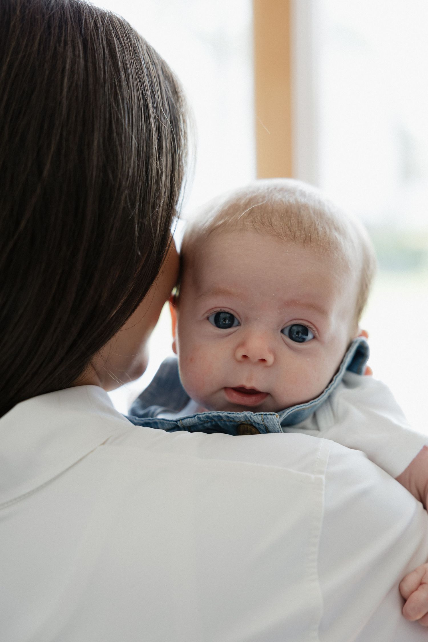 Adorable blue-eyed baby with red hair resting on mother's shoulder looking at camera.