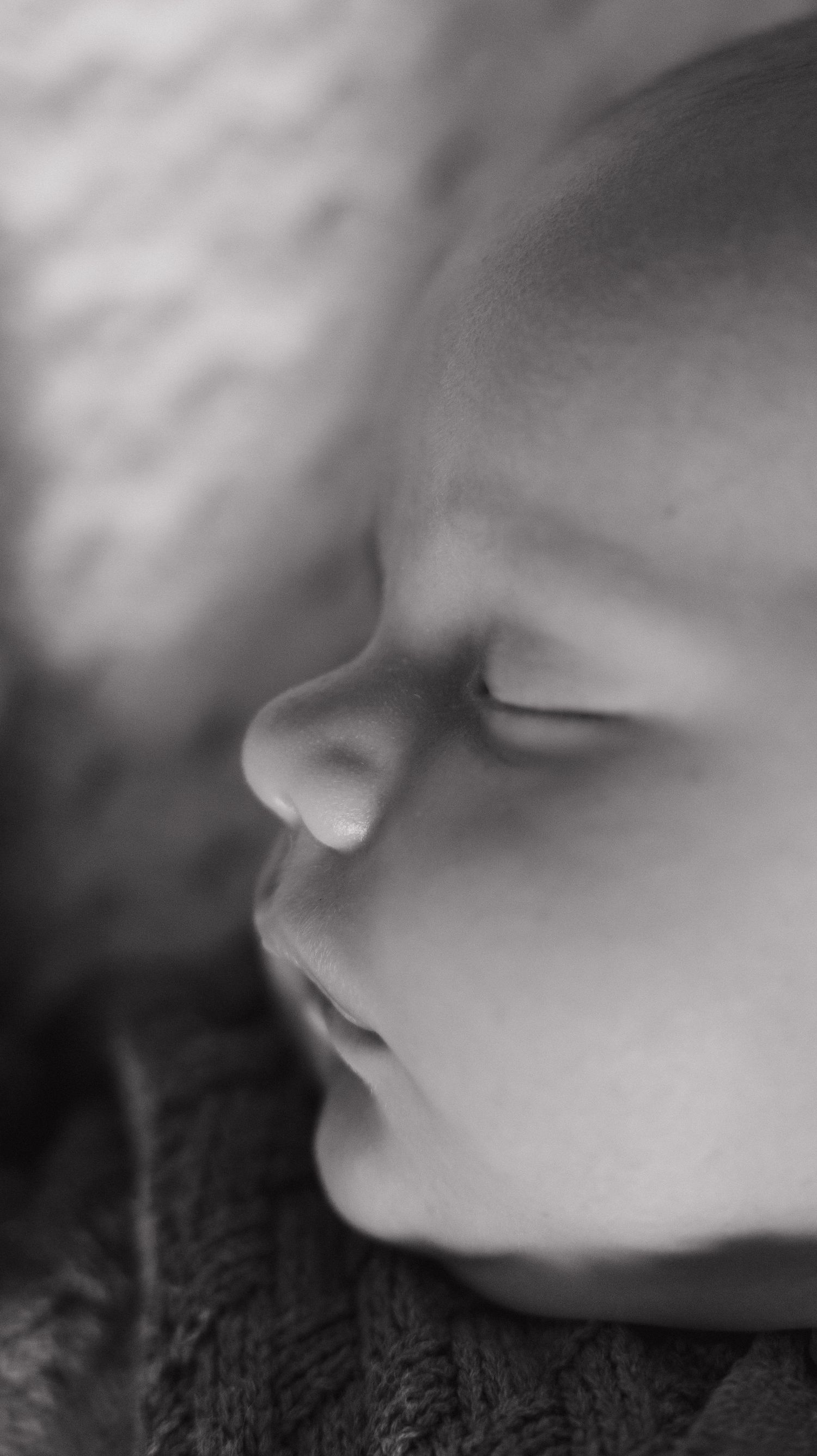 Close-up black and white portrait of a peacefully sleeping newborn baby's face in soft focus.