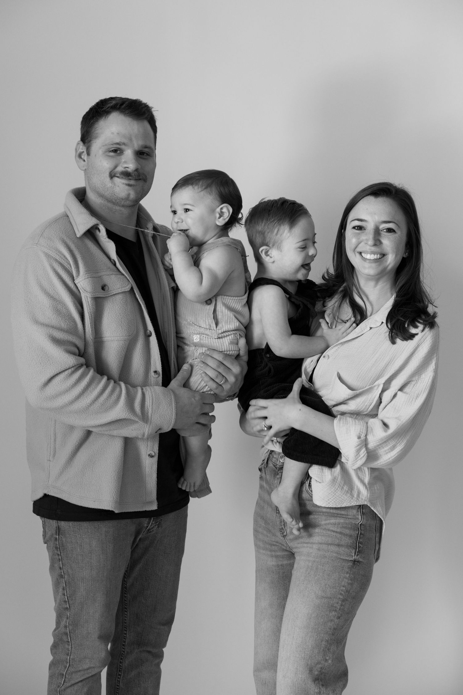 Black and white family portrait of parents holding two toddlers against a light background.