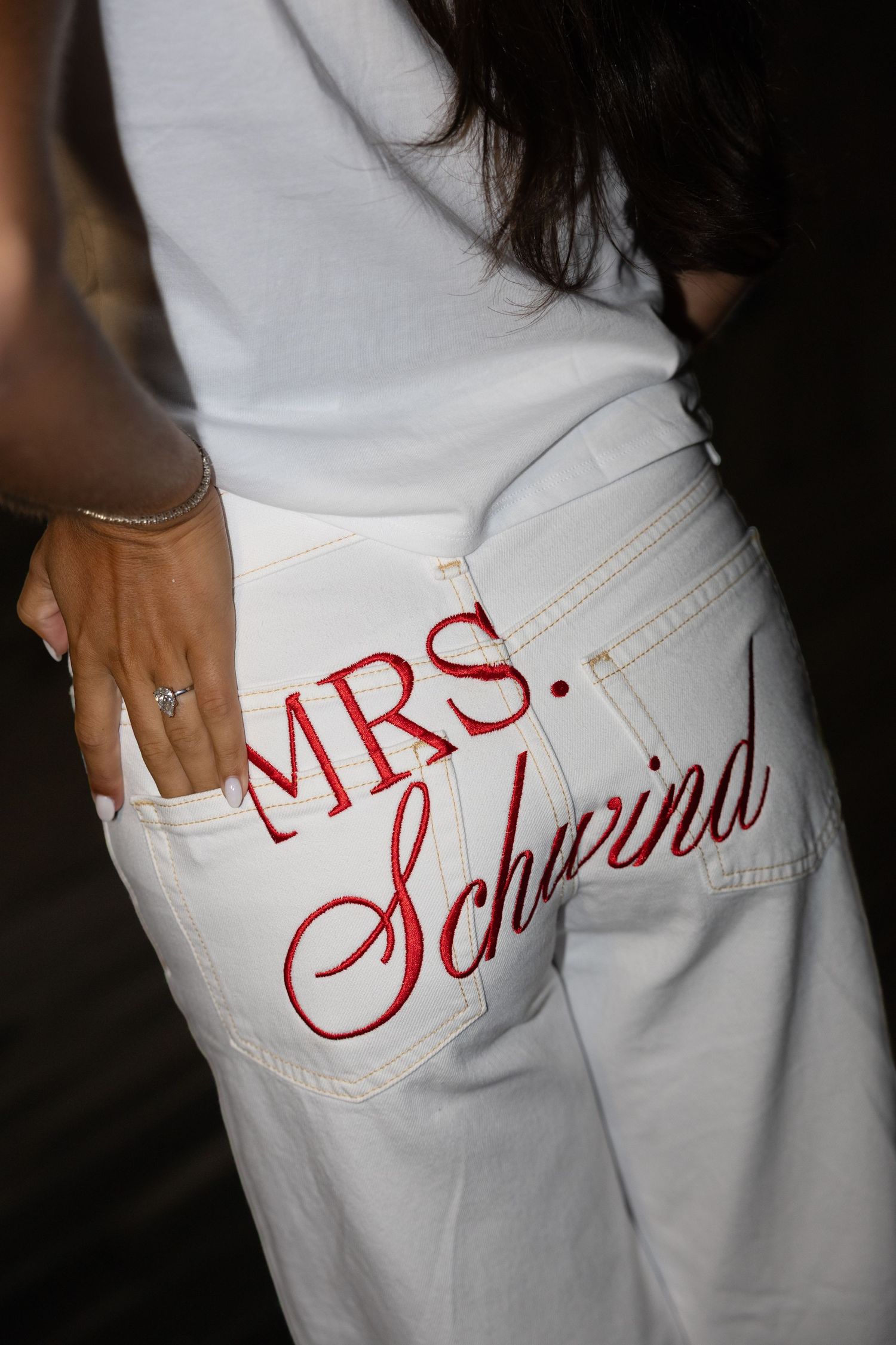 White jeans with red embroidered Mrs. Schwrina text on back pocket, worn by a bride at a wedding.