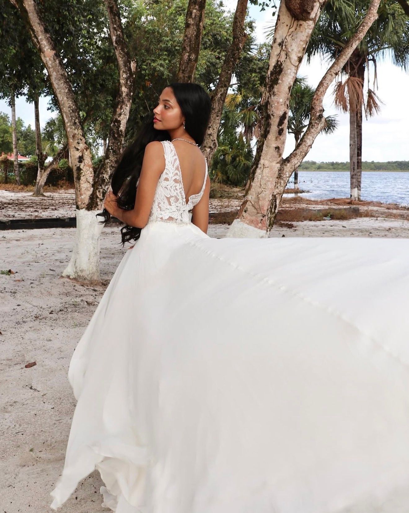 A flowing white wedding dress photographed on a tropical beach with palm trees and sand.