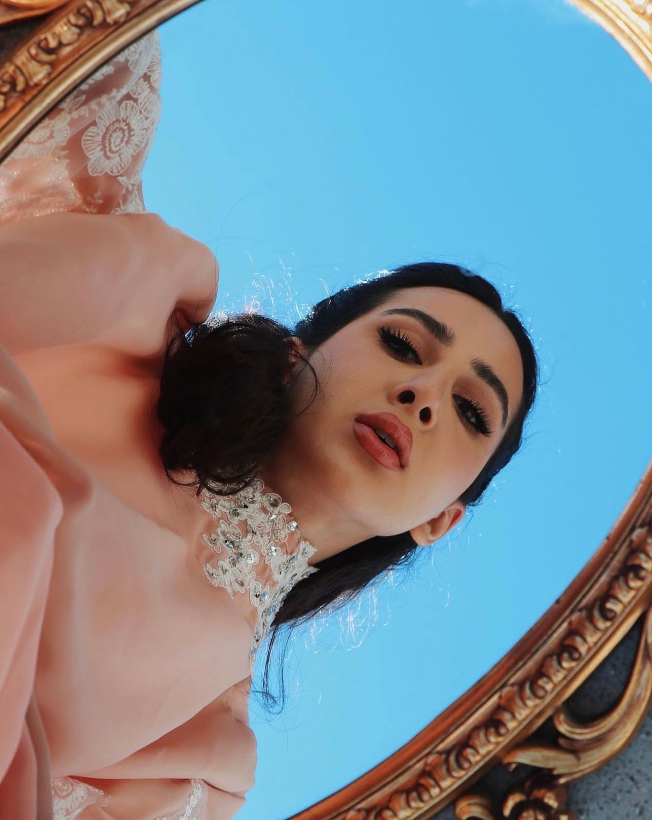 Artistic portrait shot looking up at a figure against blue sky with ornate gold frame details in view.