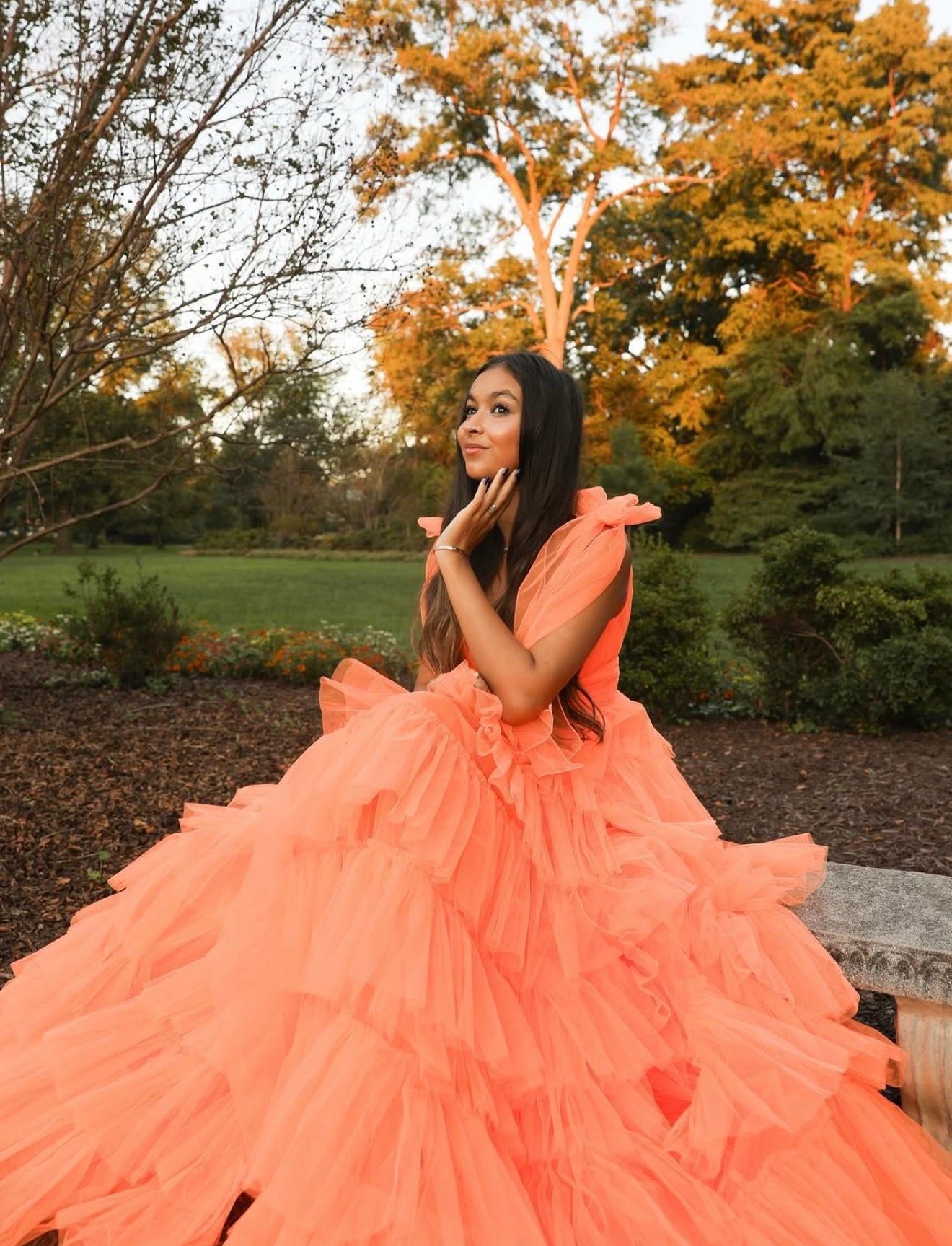 Flowing coral orange ballgown dress photographed in autumn park setting.