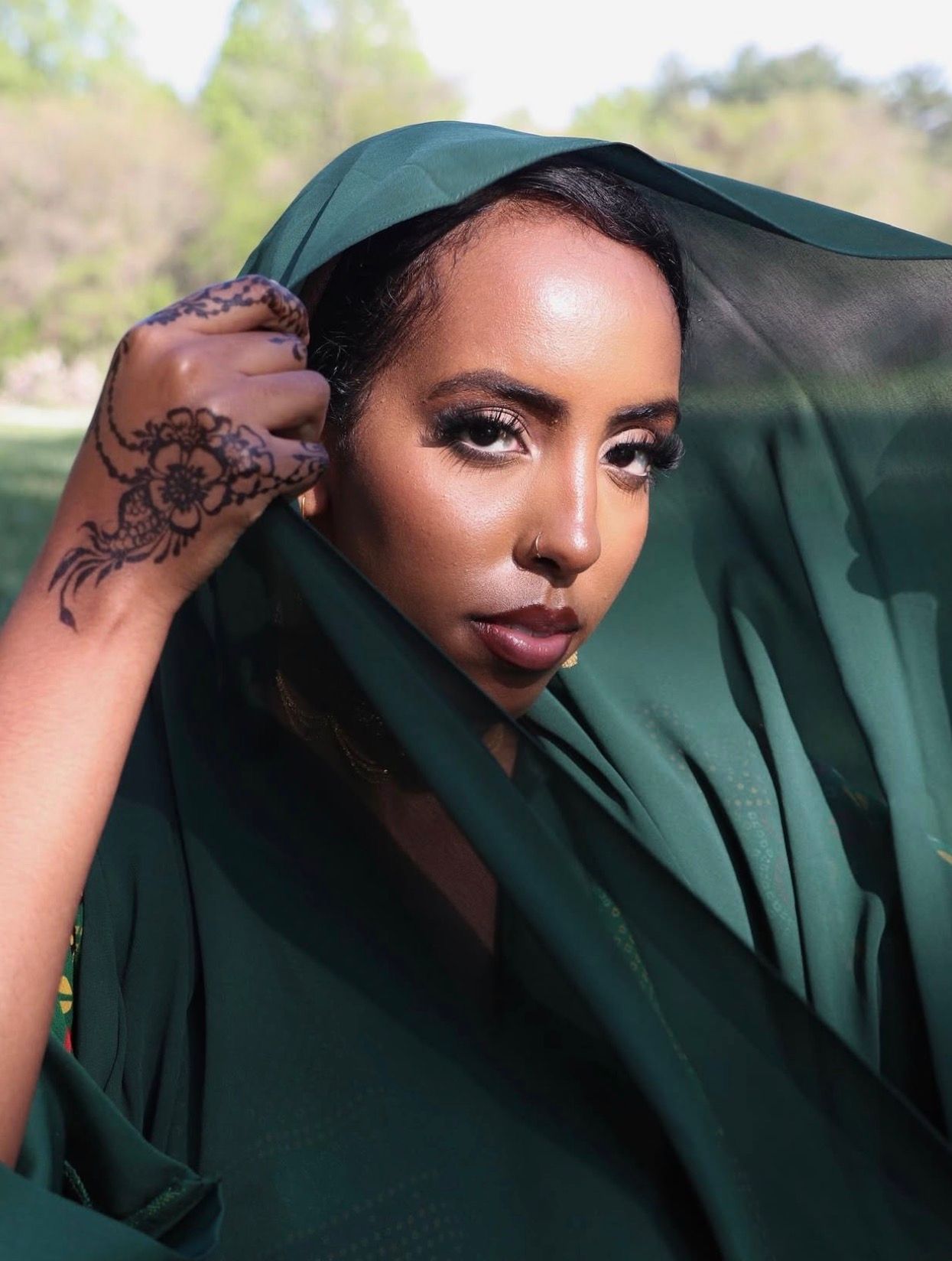 Fashion portrait series in emerald green outfit with artistic makeup and henna details.