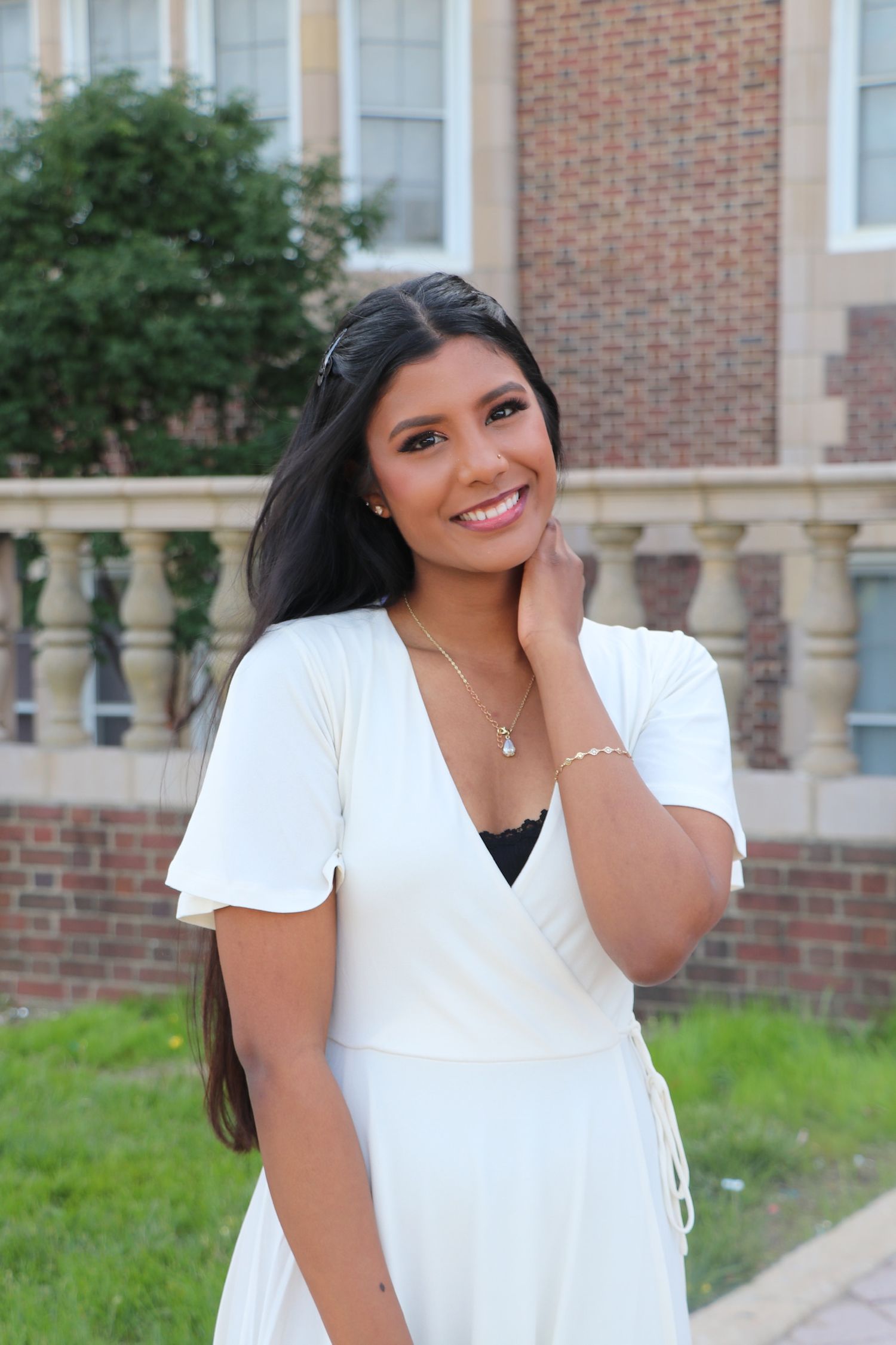 Graduate in white dress poses outdoors against brick building backdrop.