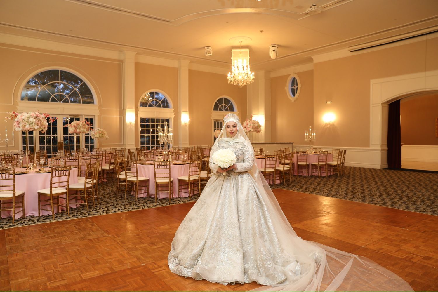 Spacious ballroom with hardwood floors and elegant lighting ready for a wedding reception.