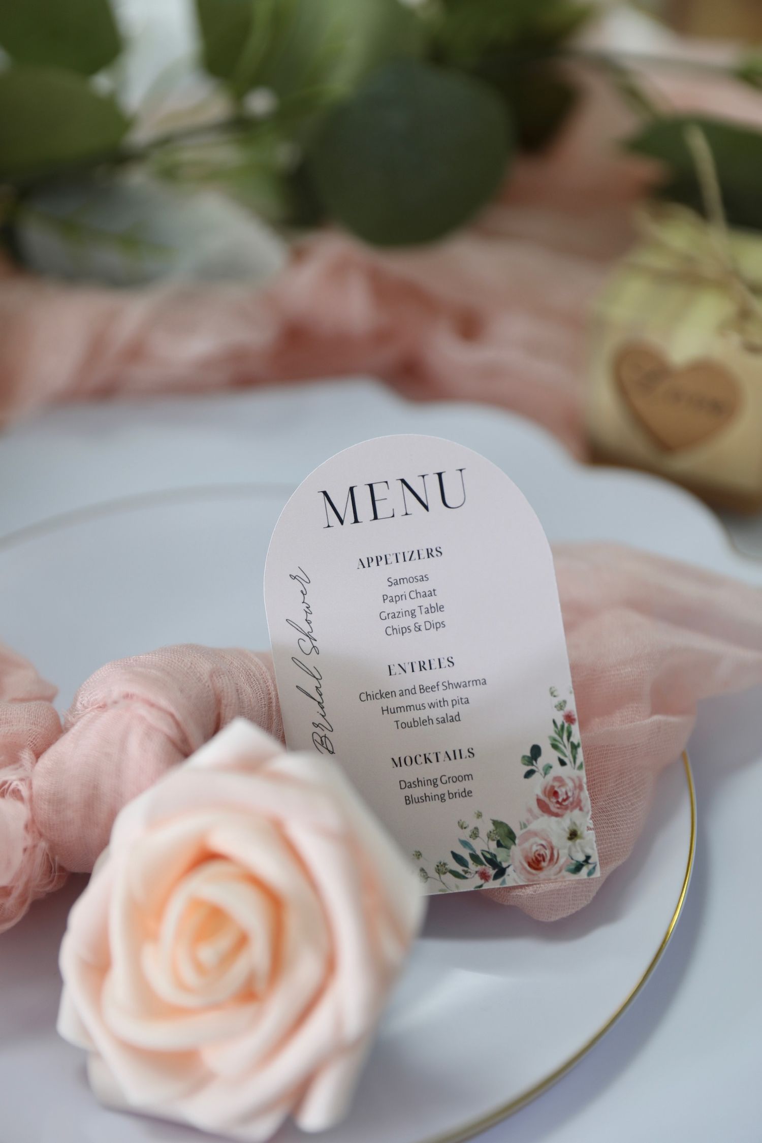 Elegant wedding menu cards with delicate pink roses and floral designs displayed on white table settings.