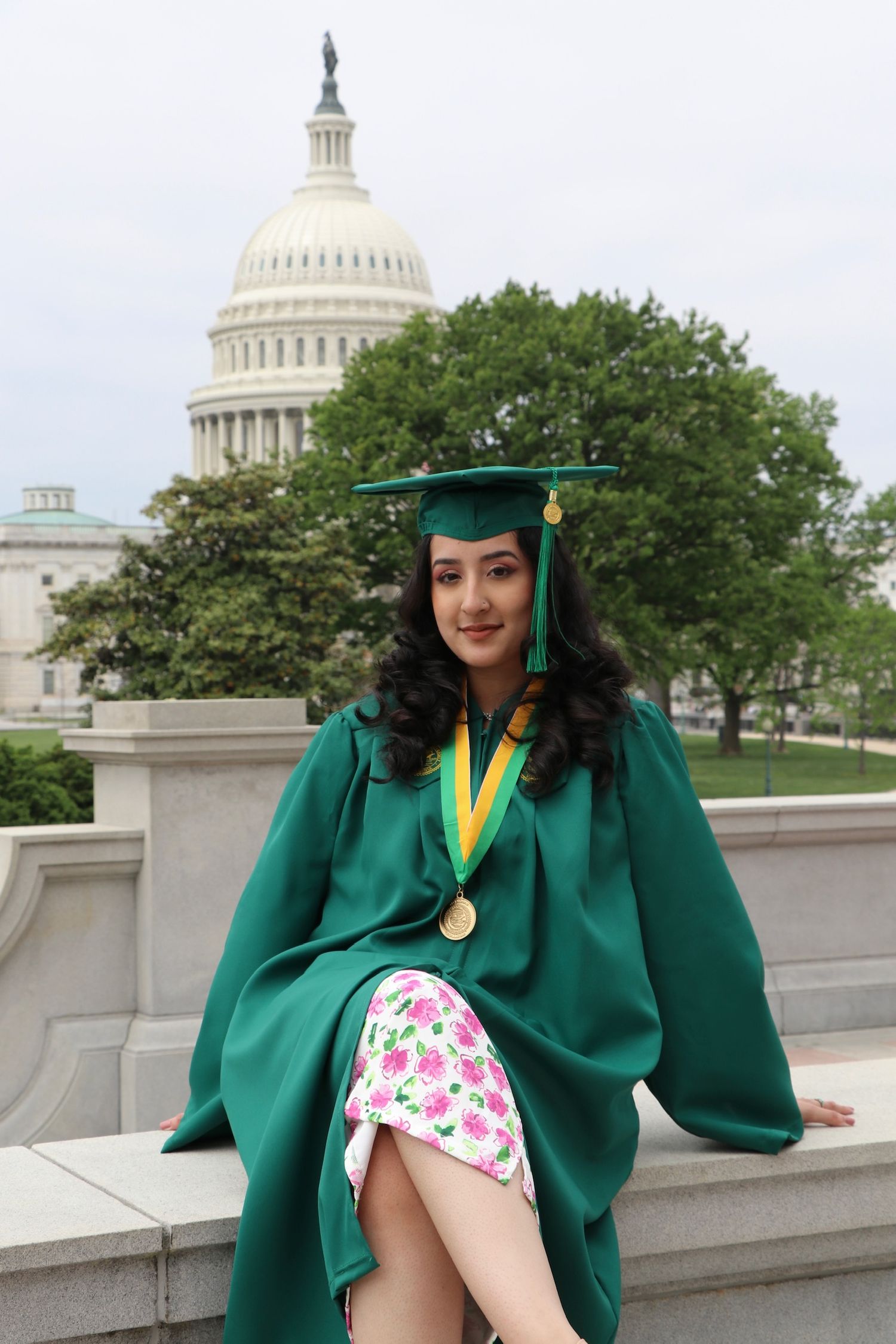 Graduate in emerald green cap and gown poses near US Capitol building.