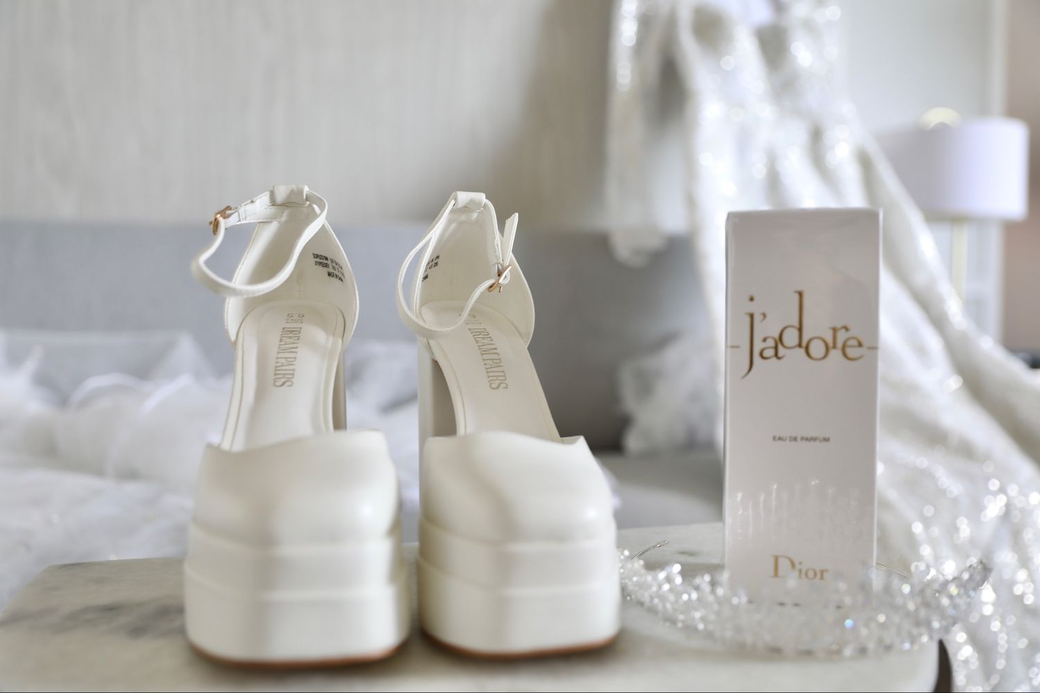 White wedding shoes and accessories arranged on a marble surface with delicate decor elements and soft lighting.