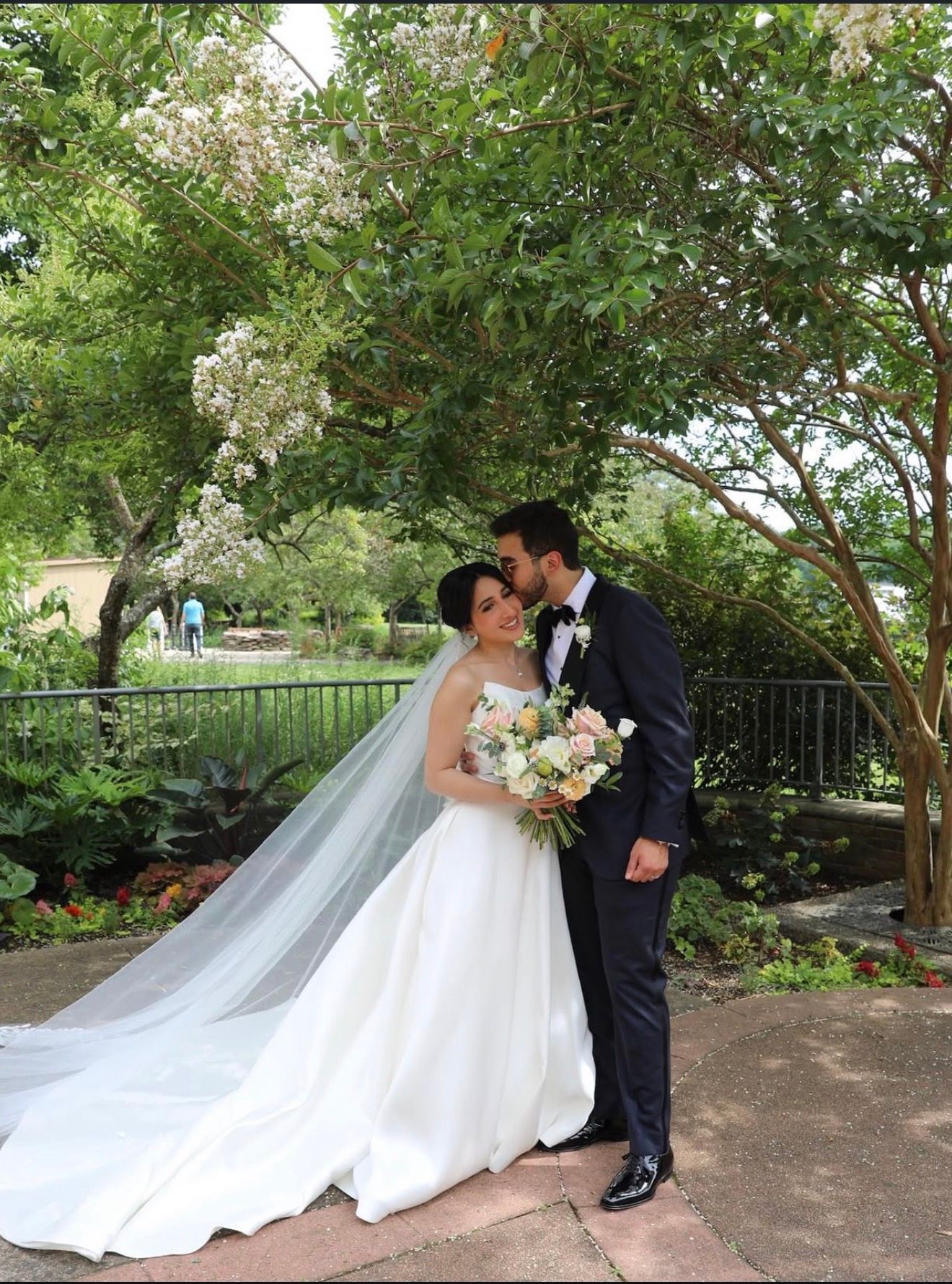 Wedding couple shares intimate moment in garden setting with flowing white dress.