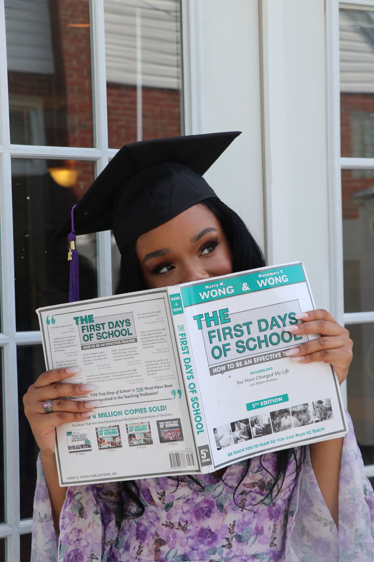 Graduates in black caps and gowns holding up books titled 'The First Days of School' during a photo session.