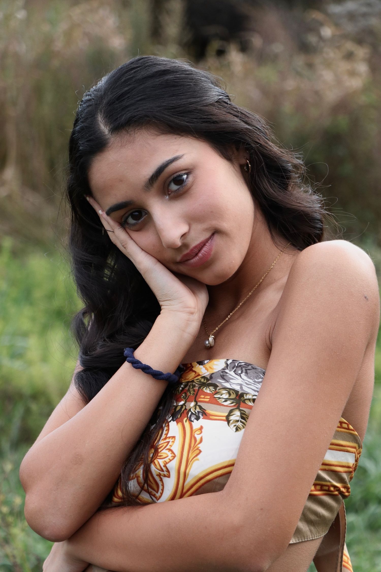 A portrait of someone in a patterned strapless top with long dark hair against a natural outdoor background.