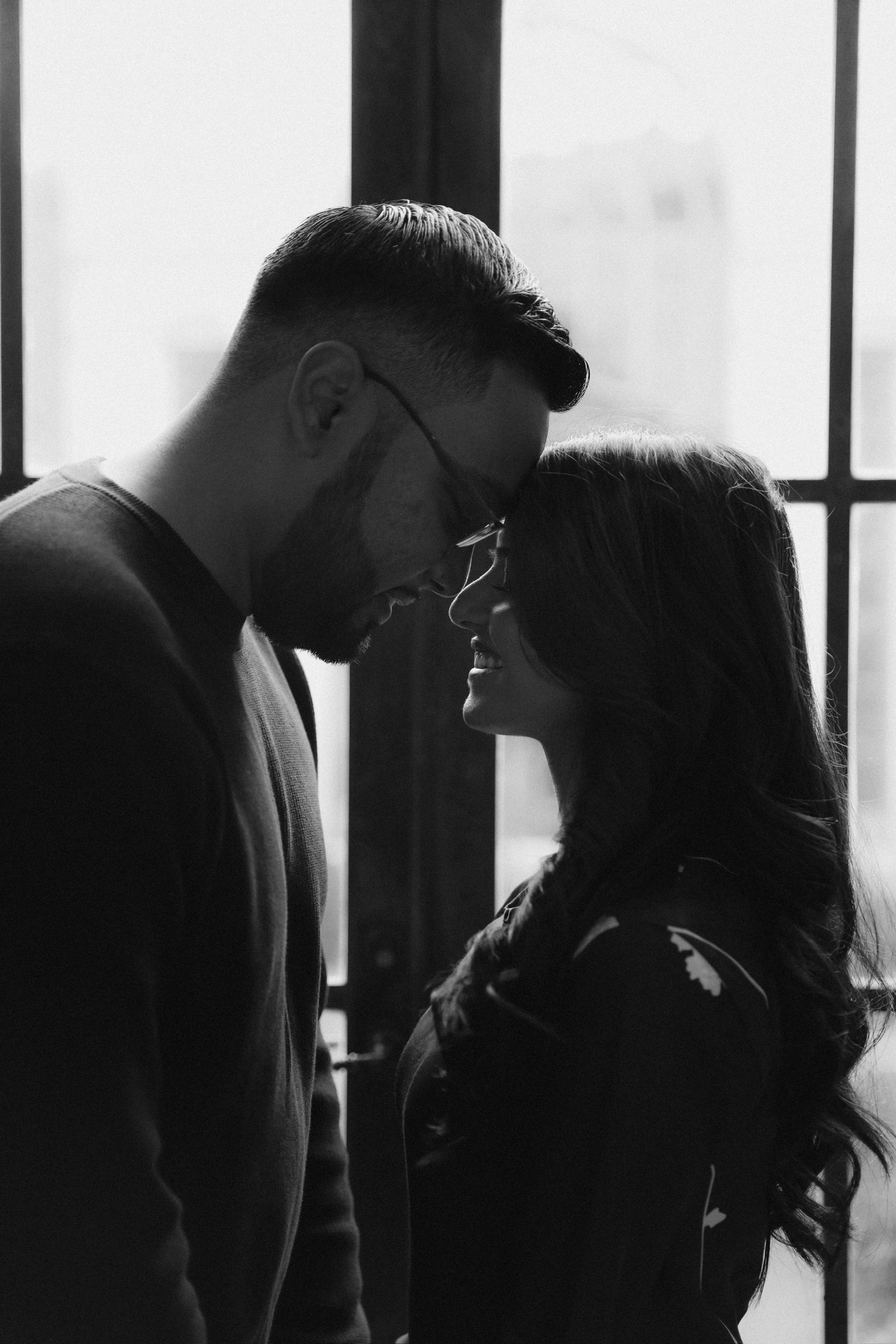 A romantic black and white silhouette of a couple sharing an intimate moment by a window.
