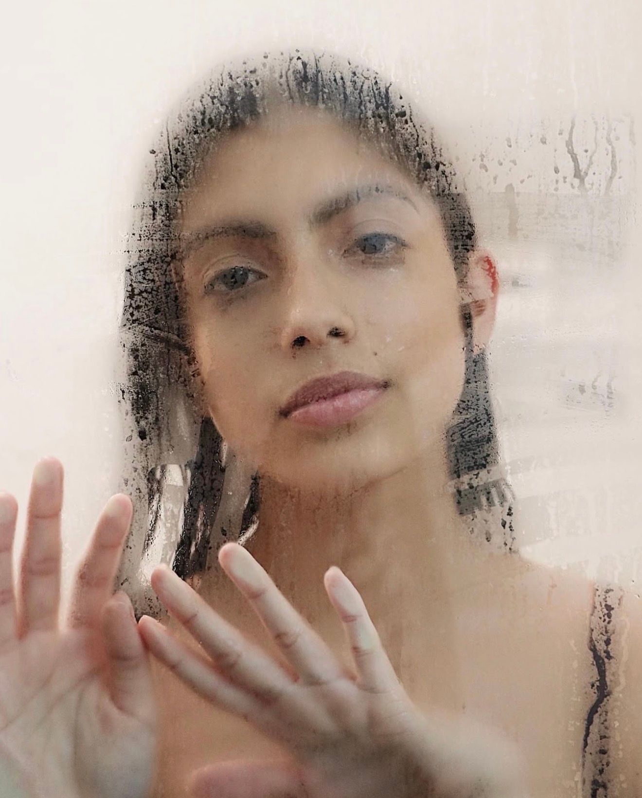 Artistic portrait through steamy glass with hands pressed against the surface creating a dreamy effect.