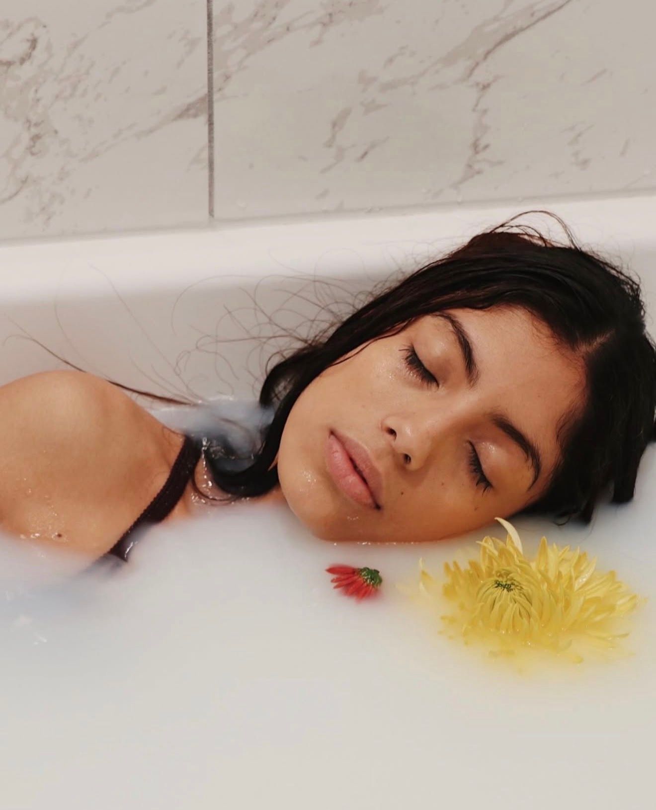 A person lies peacefully in a bathtub with yellow flowers floating in the water creating a dreamy aesthetic.