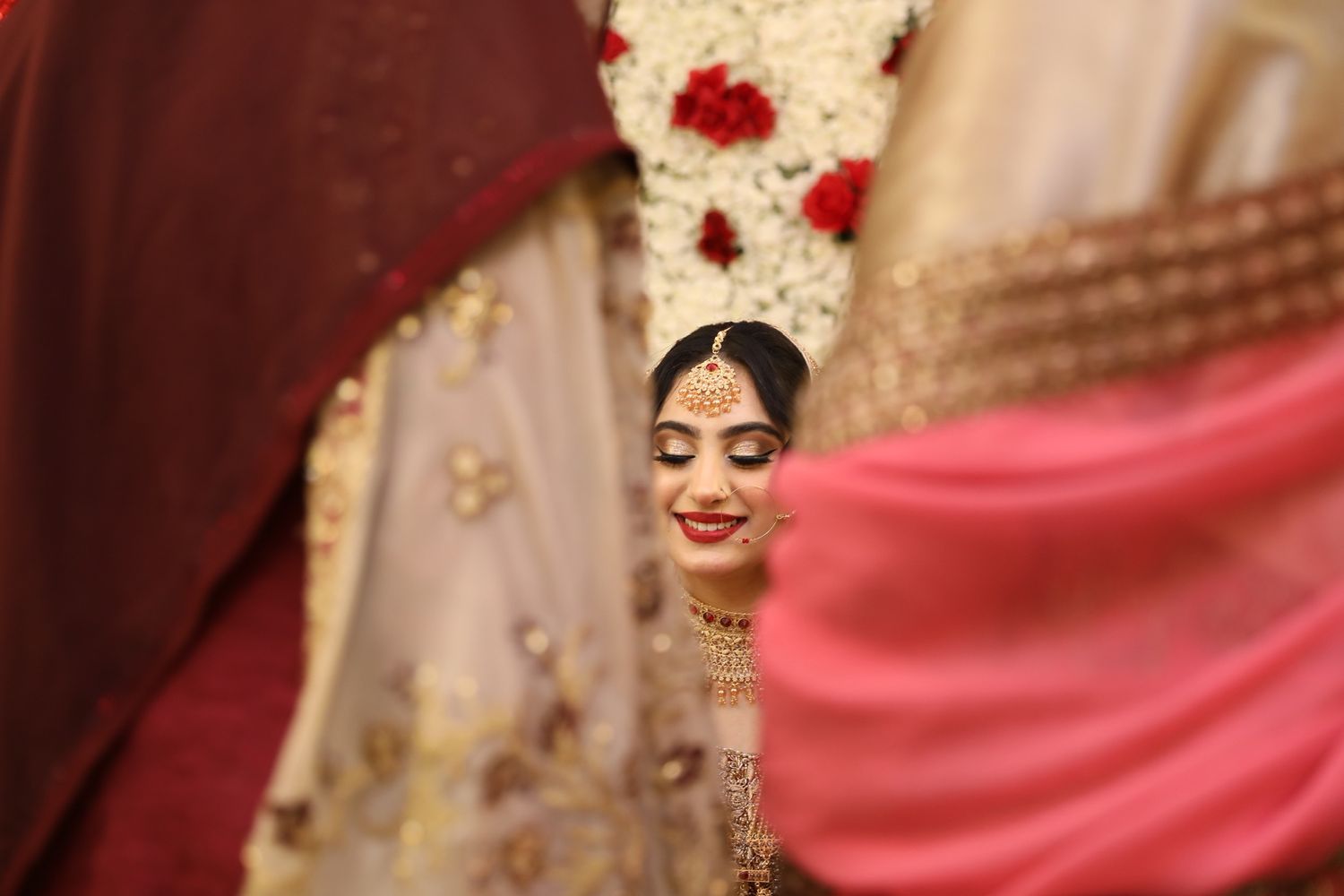 A glimpse of traditional Indian bridal beauty through flowing pink fabric at a decorated wedding ceremony.