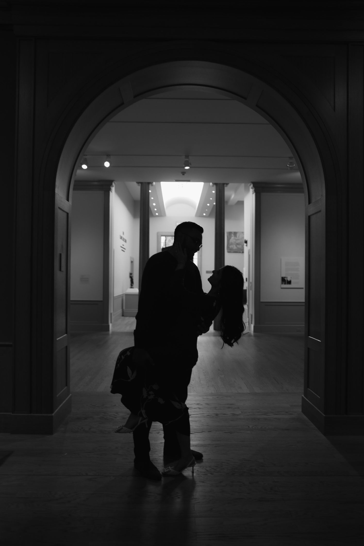 Dark silhouettes moving through an arched hallway captured in dramatic black and white photography.