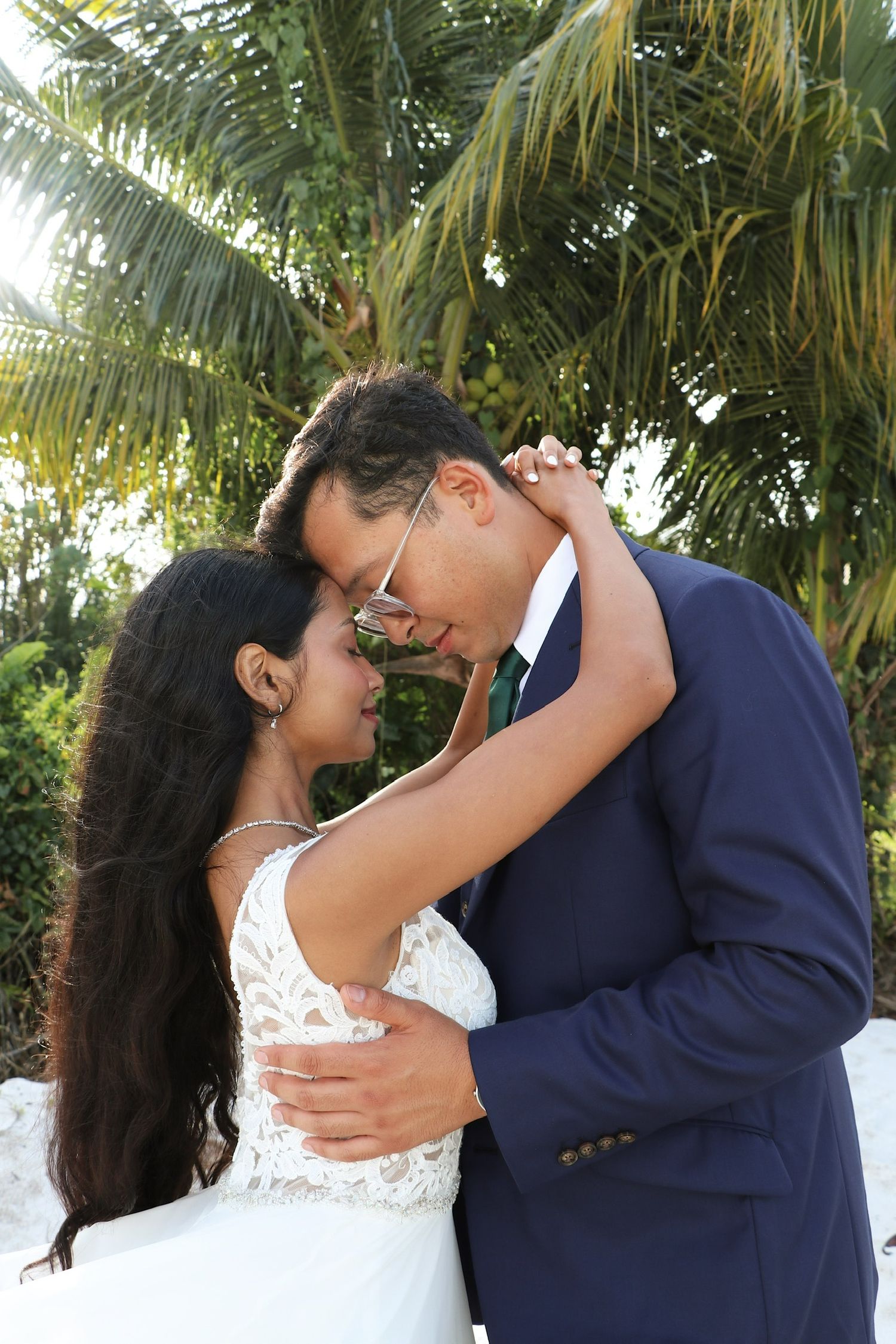 A romantic wedding couple shares an intimate dance moment under swaying palm trees in a tropical setting.