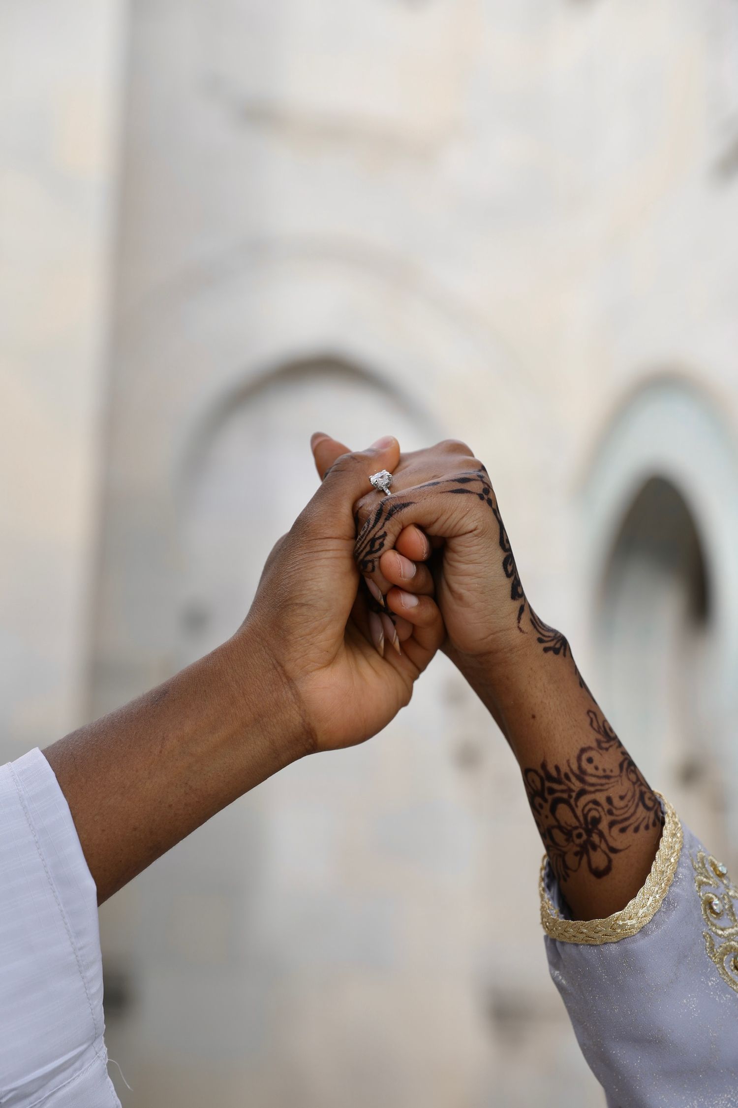 Sequence of hands with henna designs showing fist bump gestures against a blurred white architectural background.