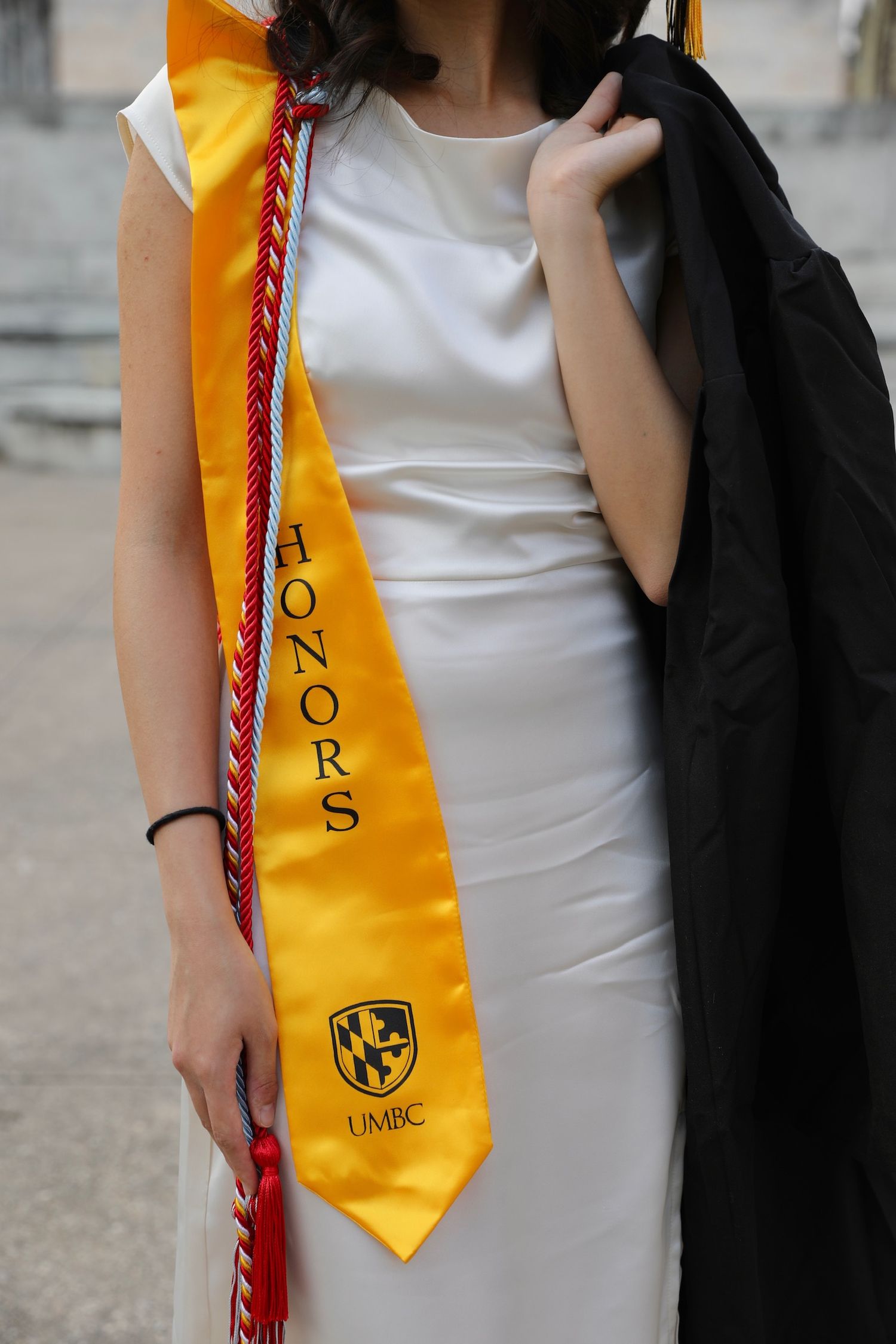 Graduate wearing white dress and gold graduation stole with university insignia during commencement ceremony.
