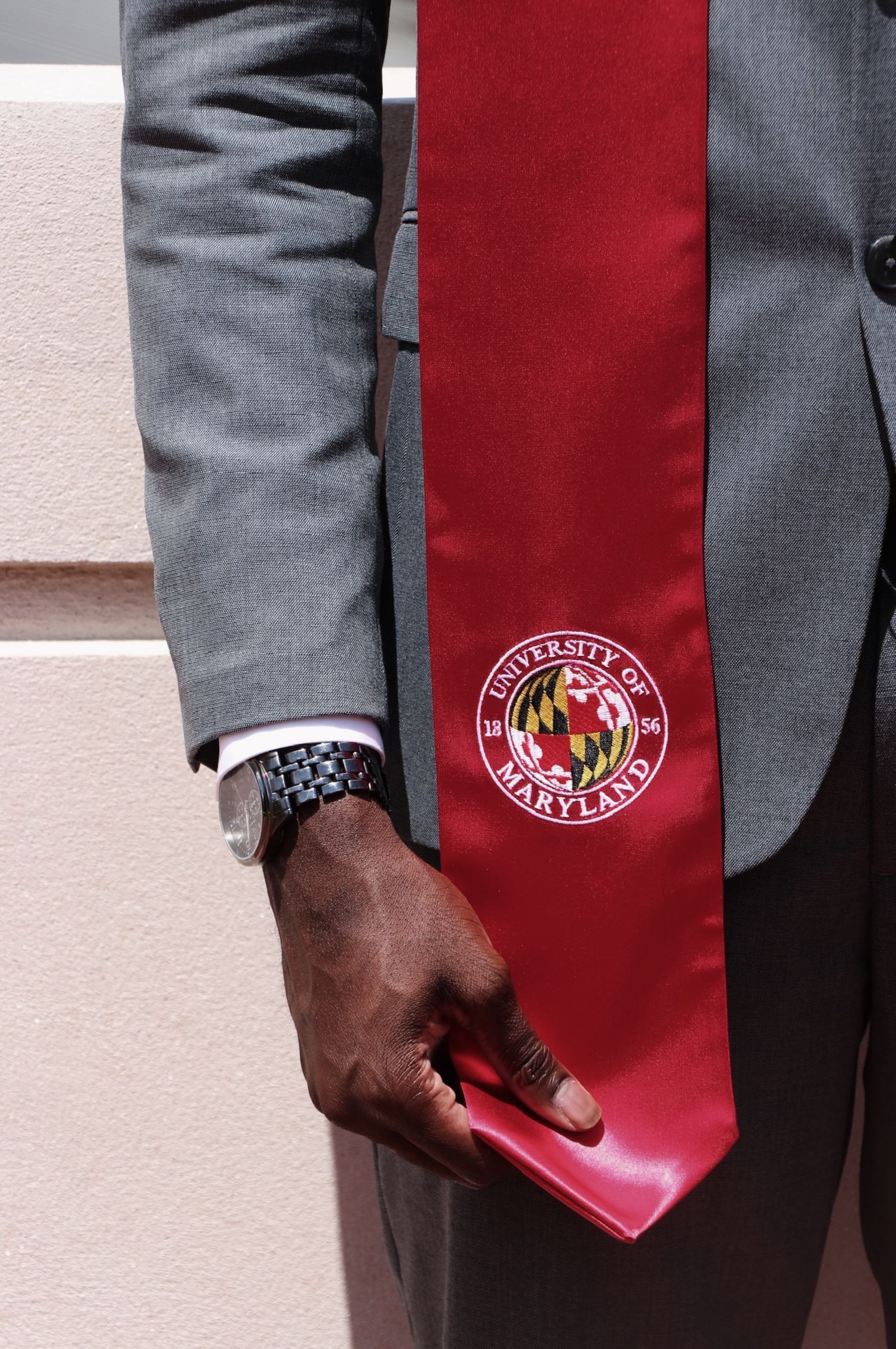 A close-up view of a person wearing a gray suit jacket and red tie with a University of Maryland logo visible.