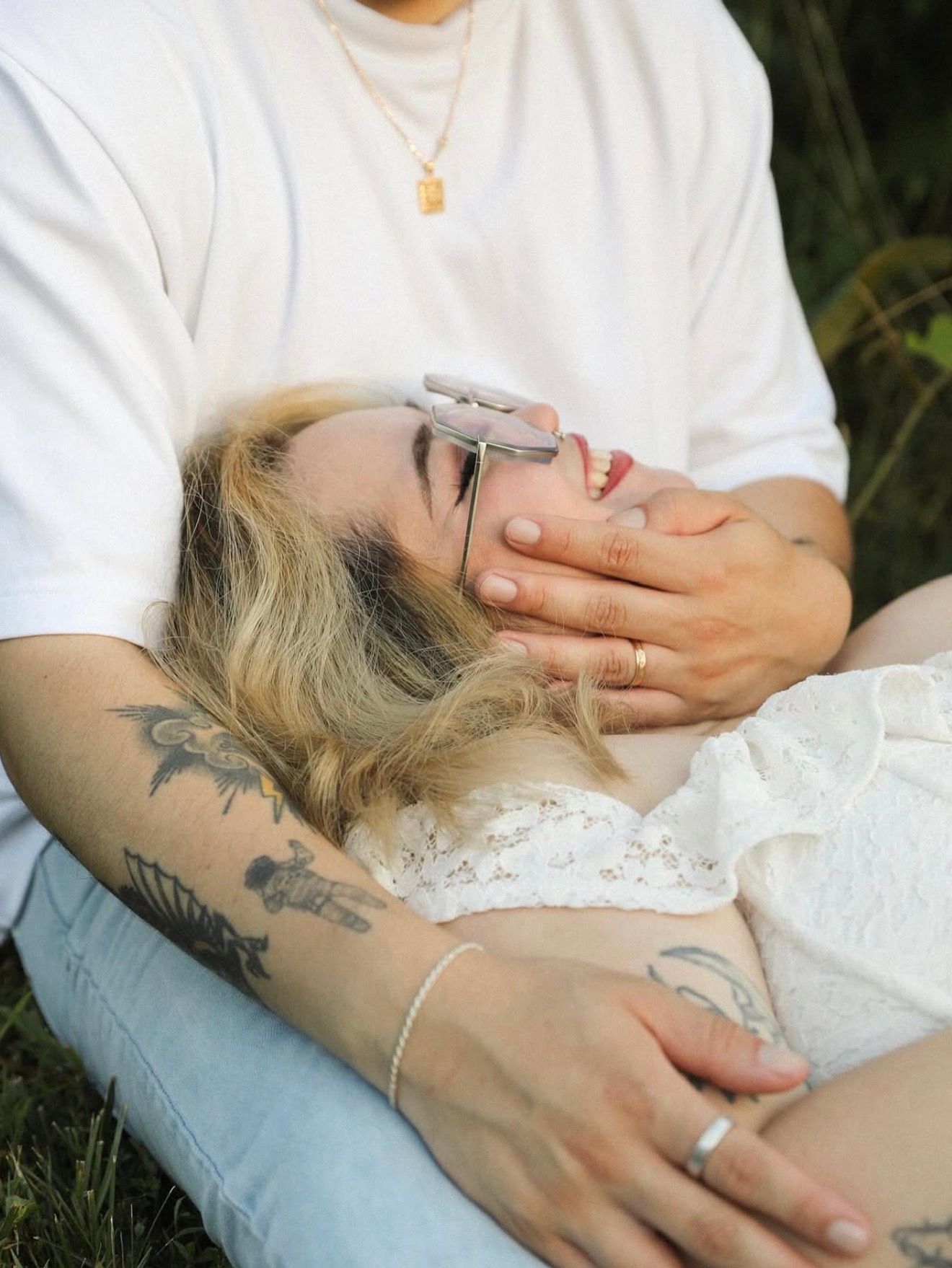 Hands with visible tattoos holding delicate white lace fabric outdoors.