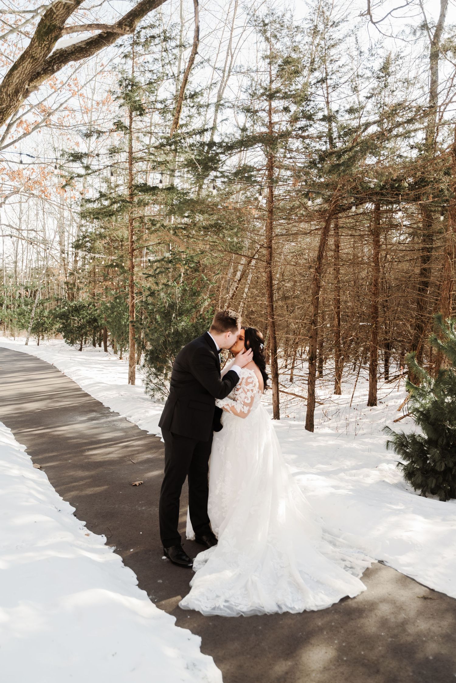 Winter wedding couple's joyful interaction on snow-covered path surrounded by pine trees.