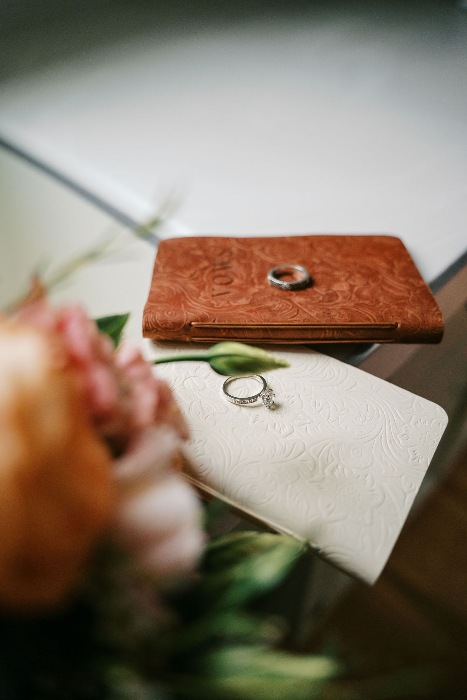 Two wedding rings resting on embossed leather journals beside a soft floral bouquet.