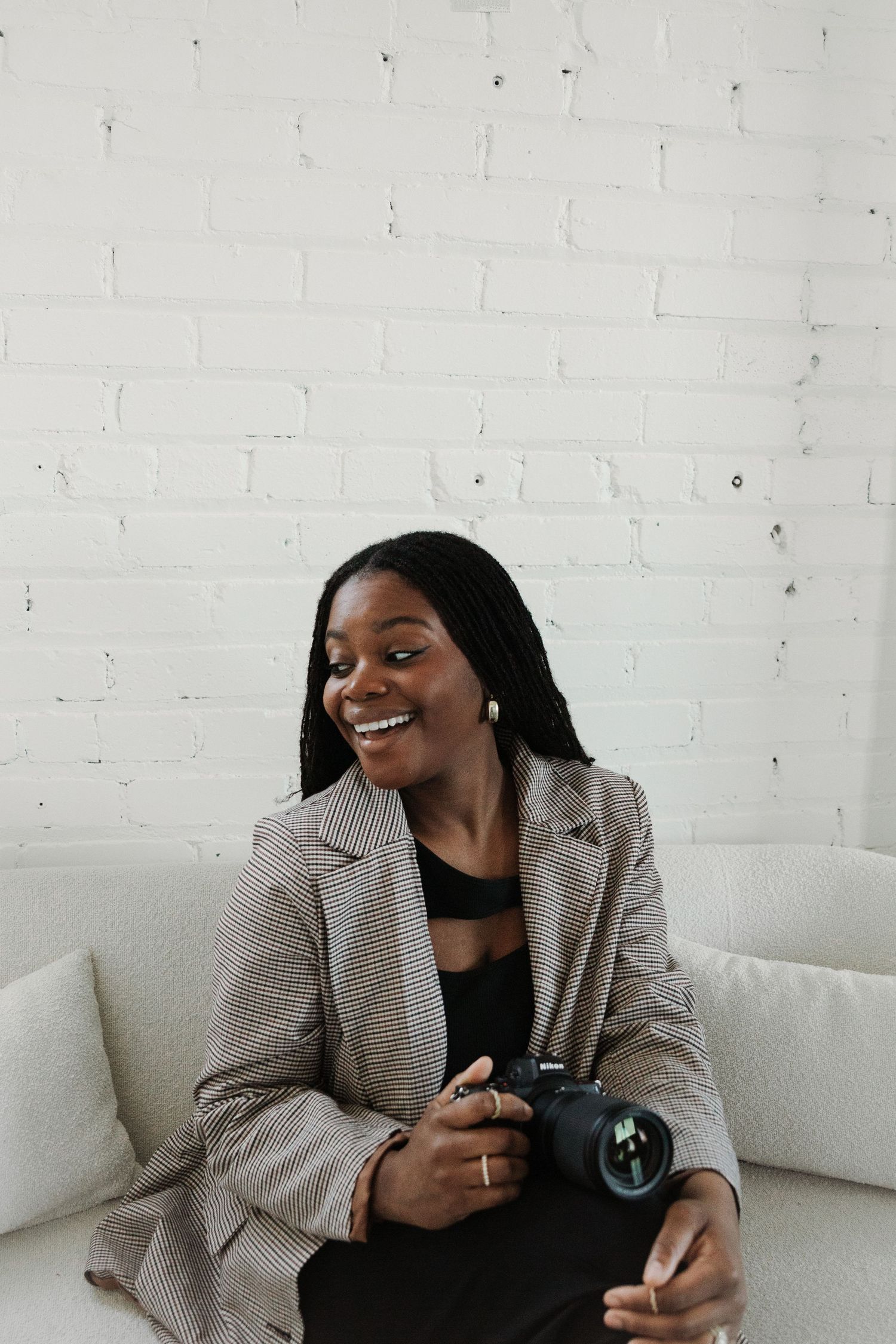 A candid sequence of someone laughing while sitting on a white couch wearing a plaid blazer.