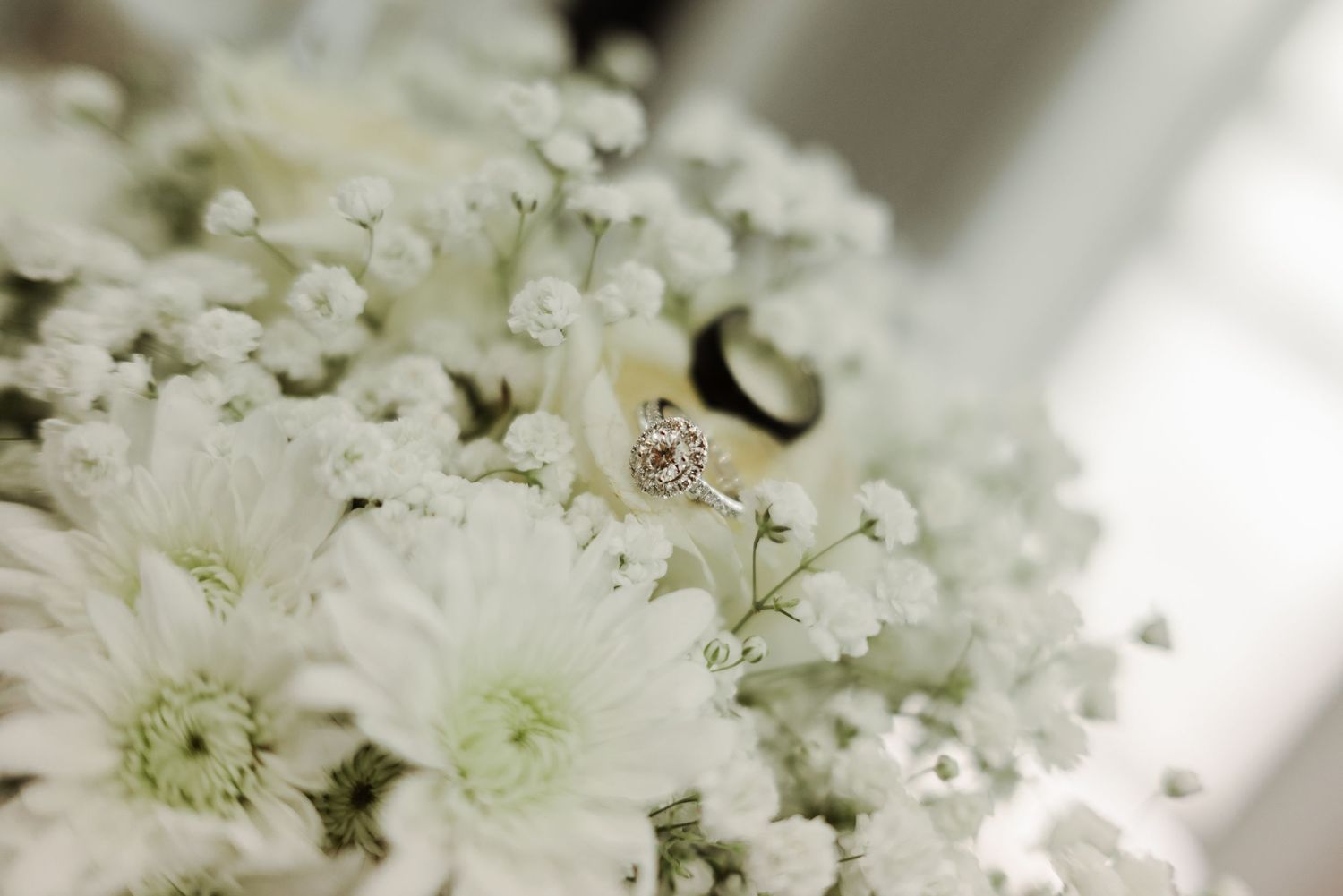 Engagement ring nestled among white flowers in a delicate wedding arrangement.