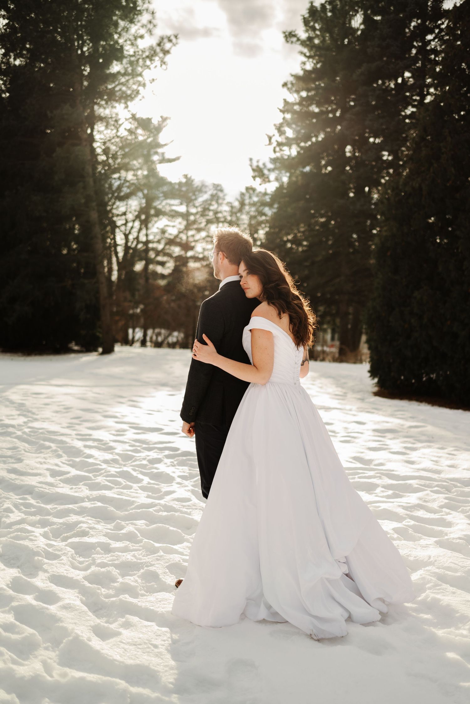 Romantic wedding portraits in a snow-covered landscape with dramatic backlighting.