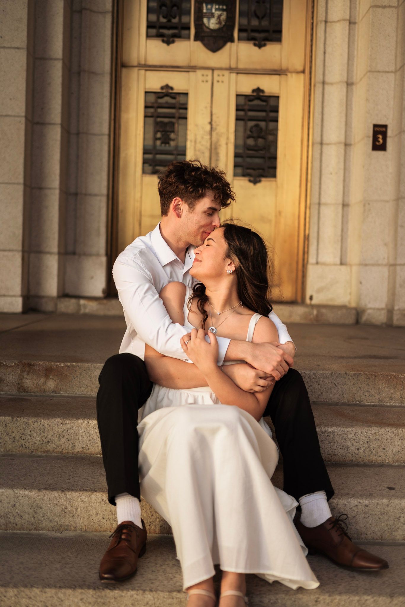 Joyful couple sharing a laugh while sitting on stone steps at sunset.