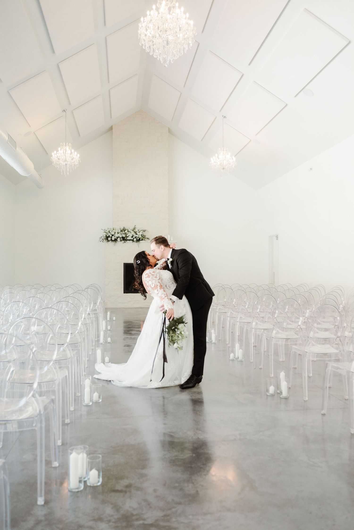 An elegant wedding venue with ghost chairs and crystal chandeliers in a modern white space.