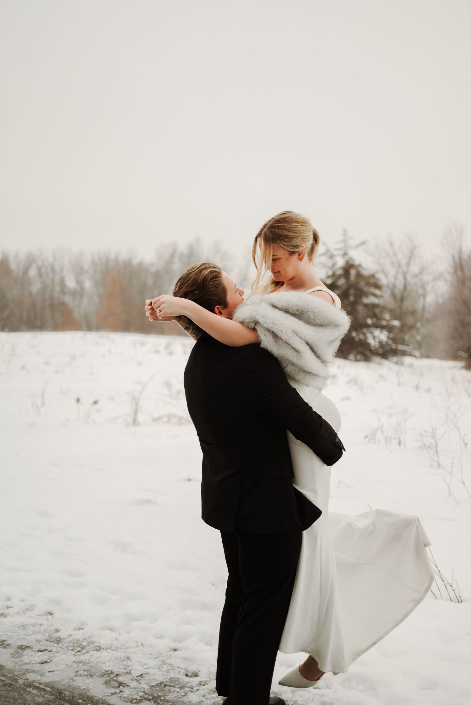 Playful winter wedding portraits with couple dancing in snowy landscape.