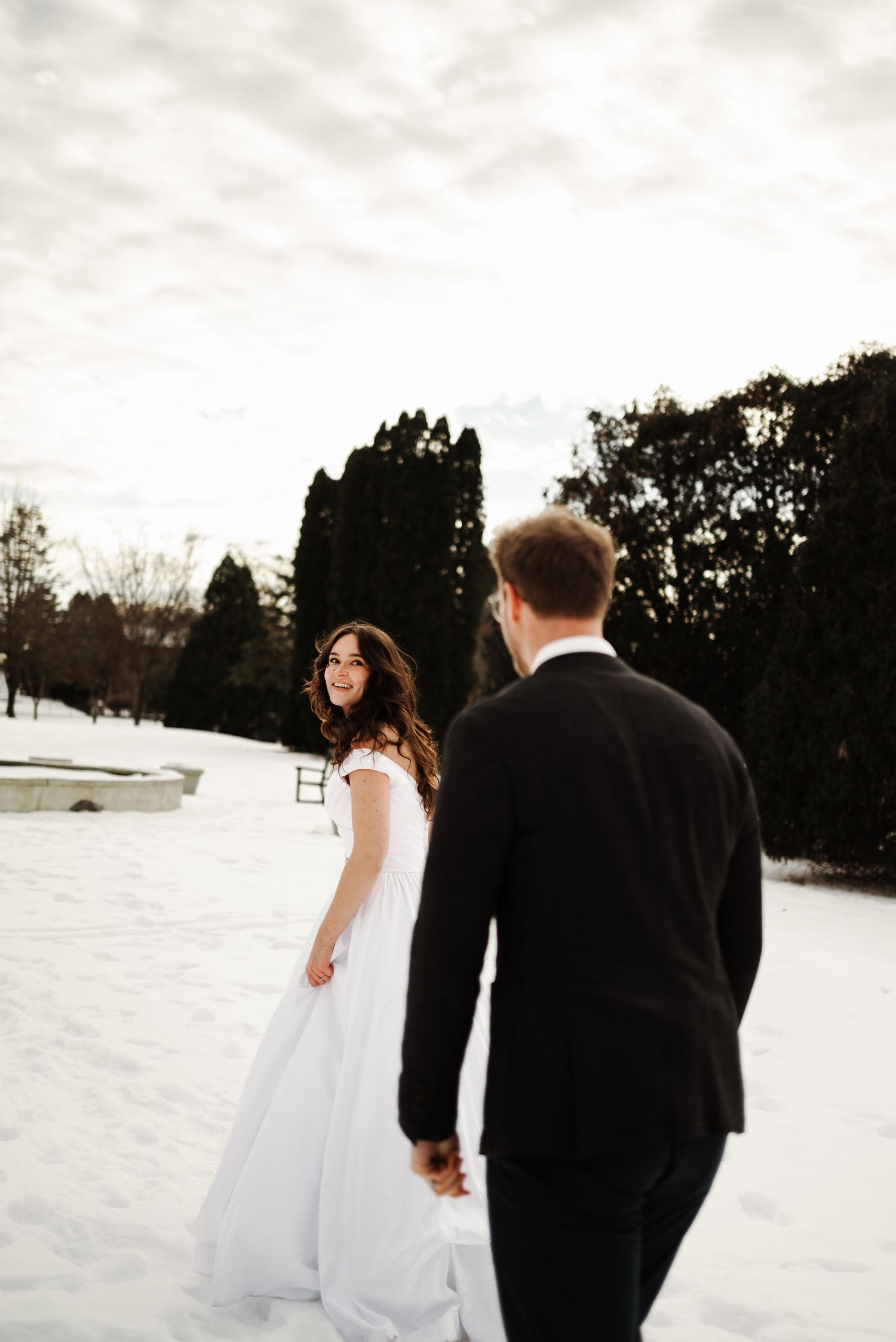 Winter wedding portrait with snow-covered landscape and moody sky backdrop.