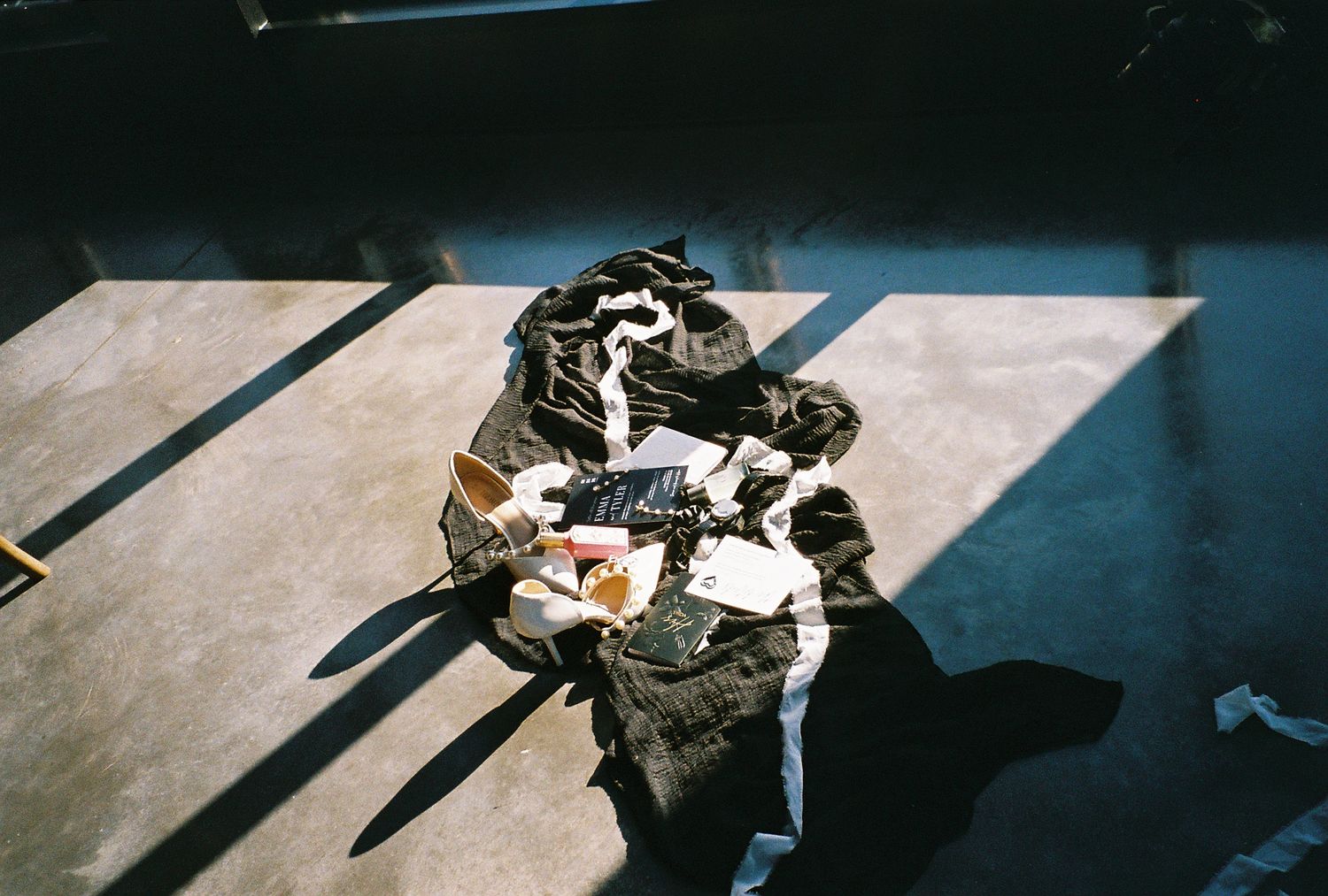 Pile of dark fabric and mixed items casting shadows on a concrete floor in natural light.