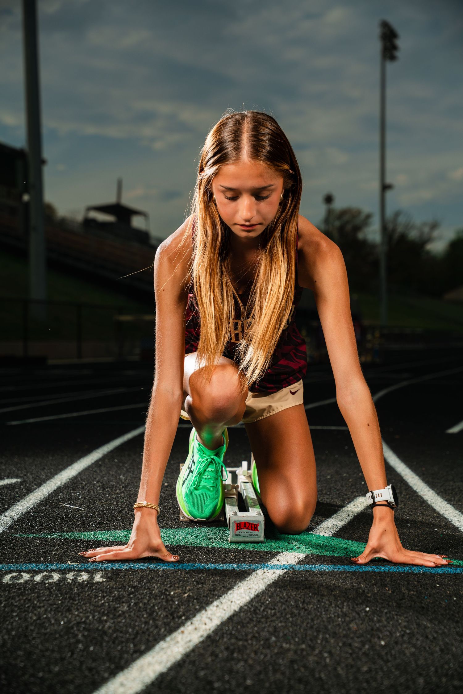 Young female athlete in starting position on a running track, wearing green sneakers and a watch, ready to sprint.