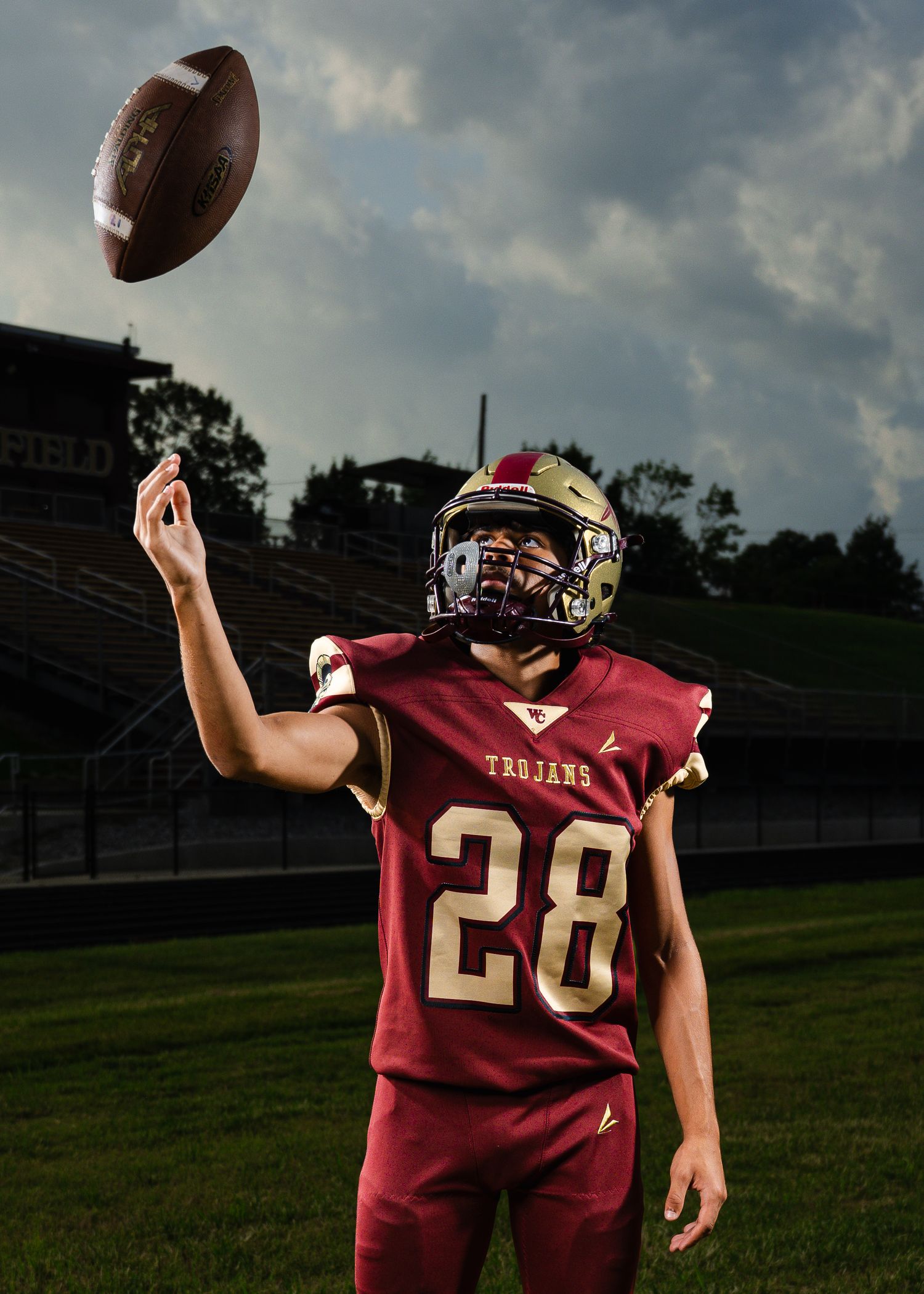 Trojans football player #28 spinning a ball on his finger in a stadium, wearing maroon uniform and helmet.